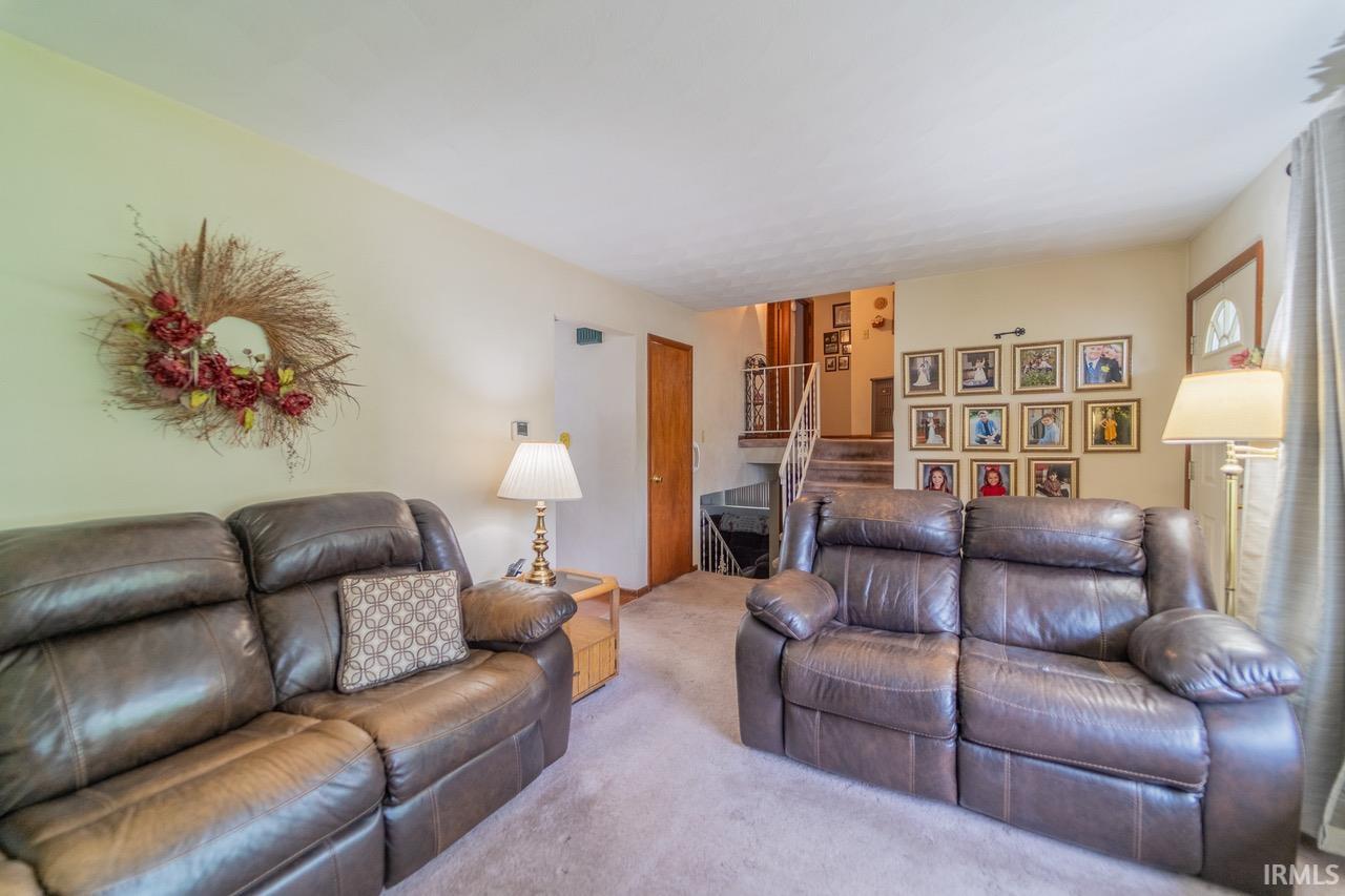 Carpeted living area featuring a wood-finish door, staircase with white railings, and light-toned walls