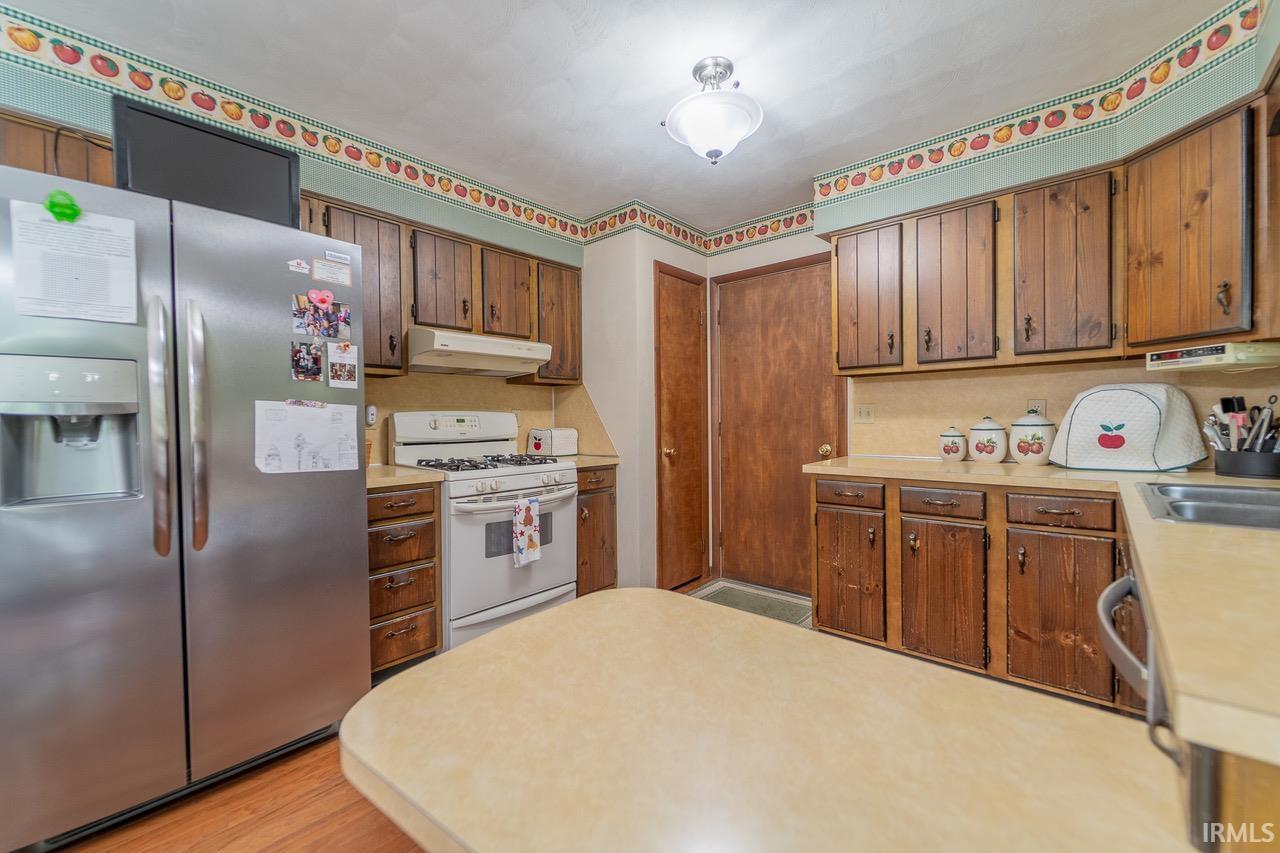 Kitchen featuring wood cabinetry, light-toned countertops, hardwood-finish flooring, a stainless steel refrigerator, and a gas range