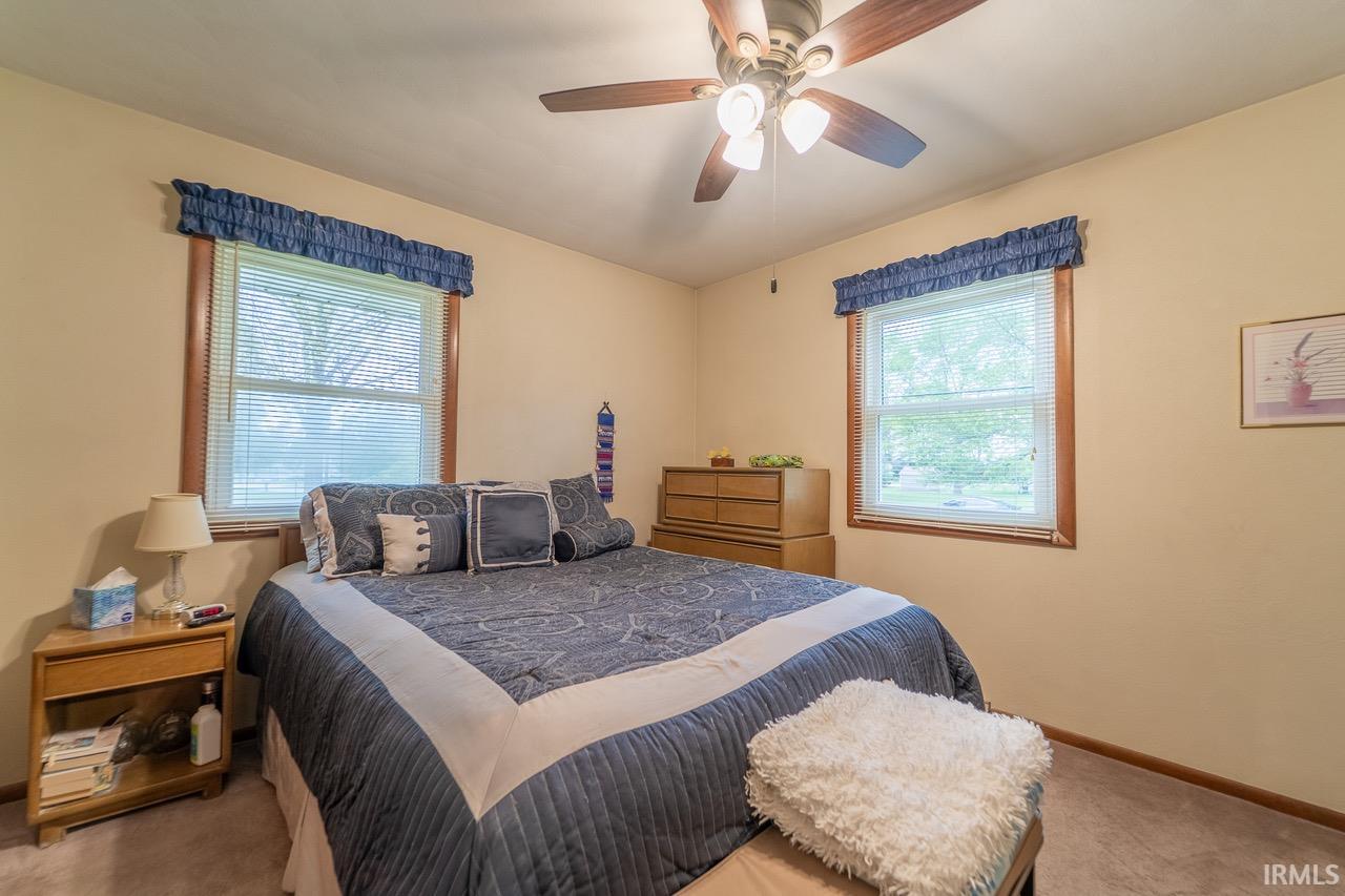 Carpeted room featuring two windows with wood trim, a ceiling fan with integrated lighting, and neutral wall tones