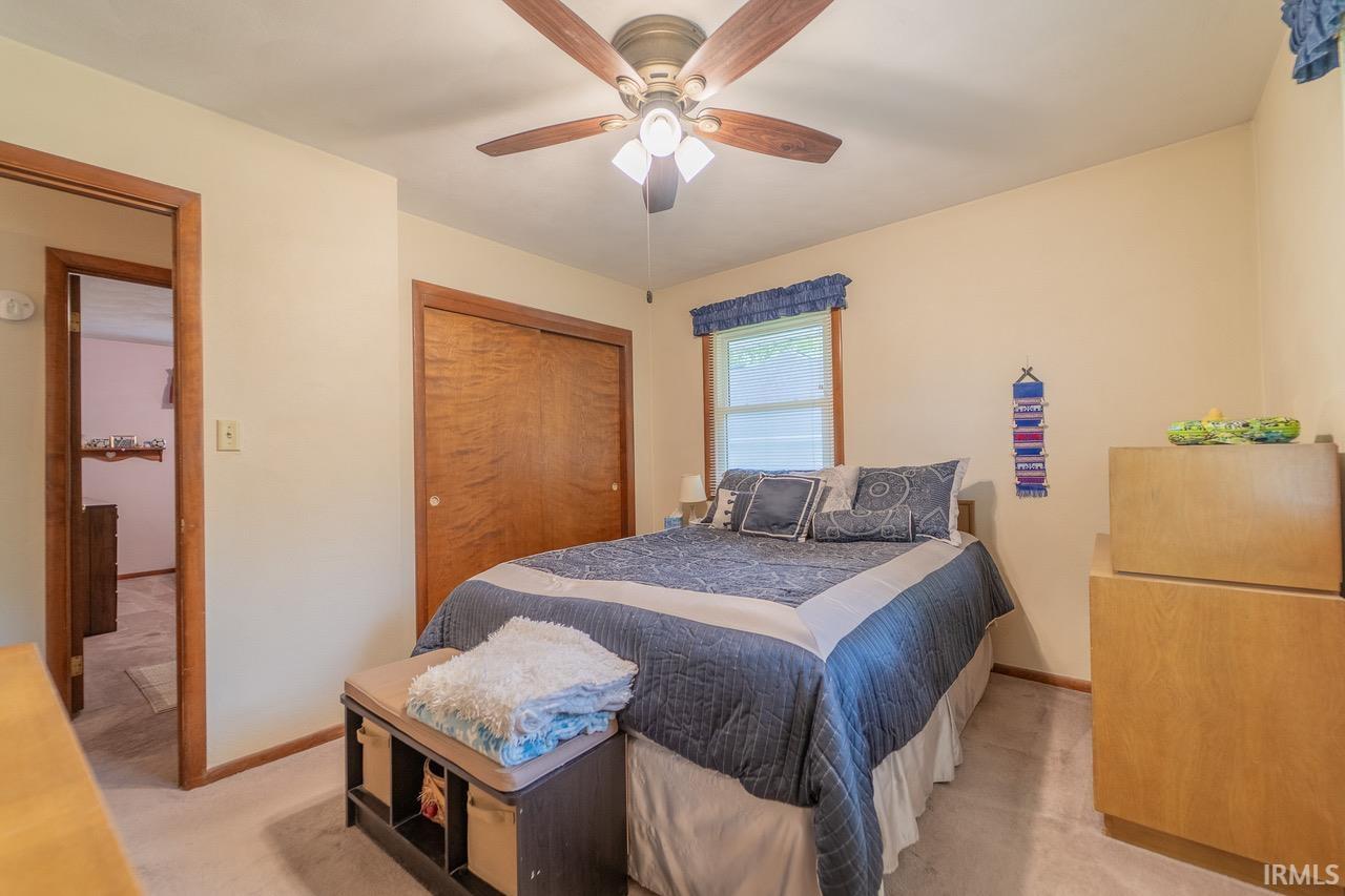 Bedroom featuring light-toned walls, a ceiling fan with light fixture, and wood-finish trim