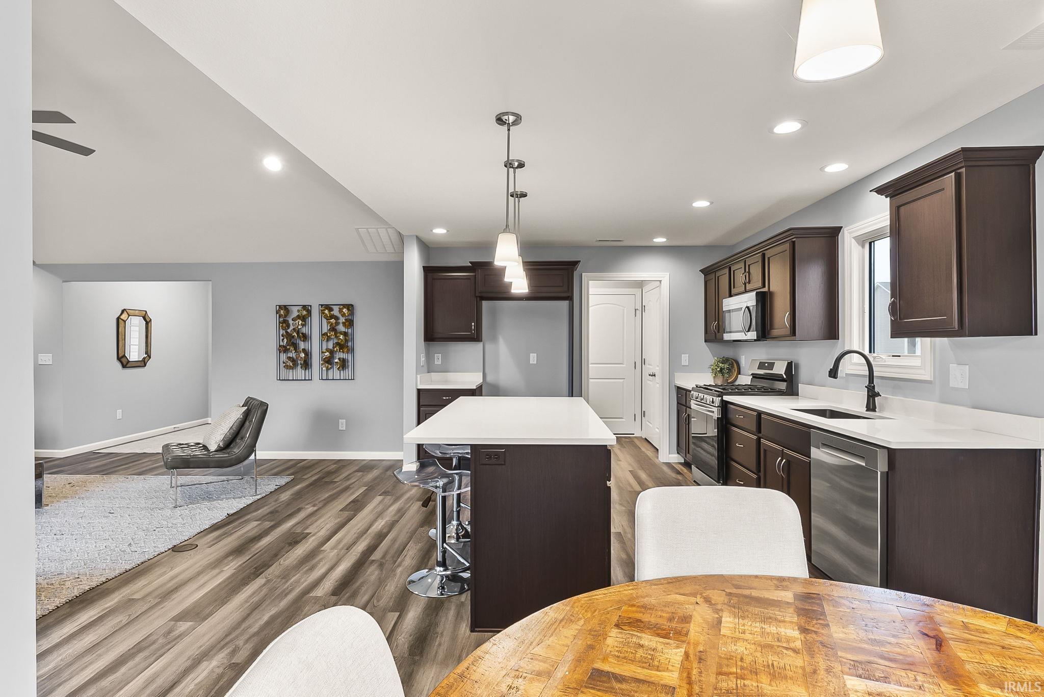Open-concept kitchen featuring dark wood cabinetry, stainless steel appliances, a center island with seating, white countertops, and wood-finish flooring