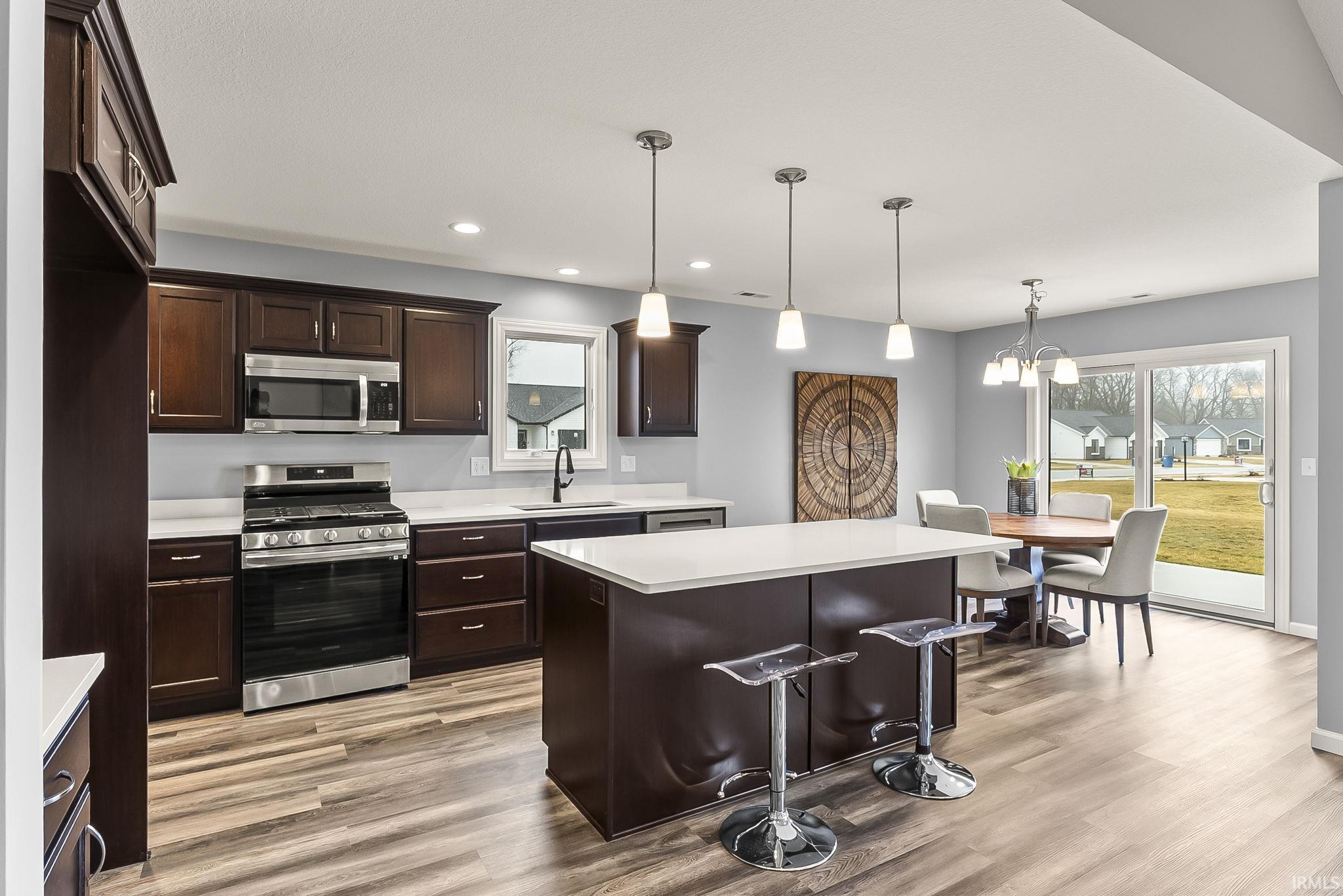 Open-concept kitchen featuring dark wood cabinetry, stainless steel appliances, a center island with a white countertop, and wood-finish flooring