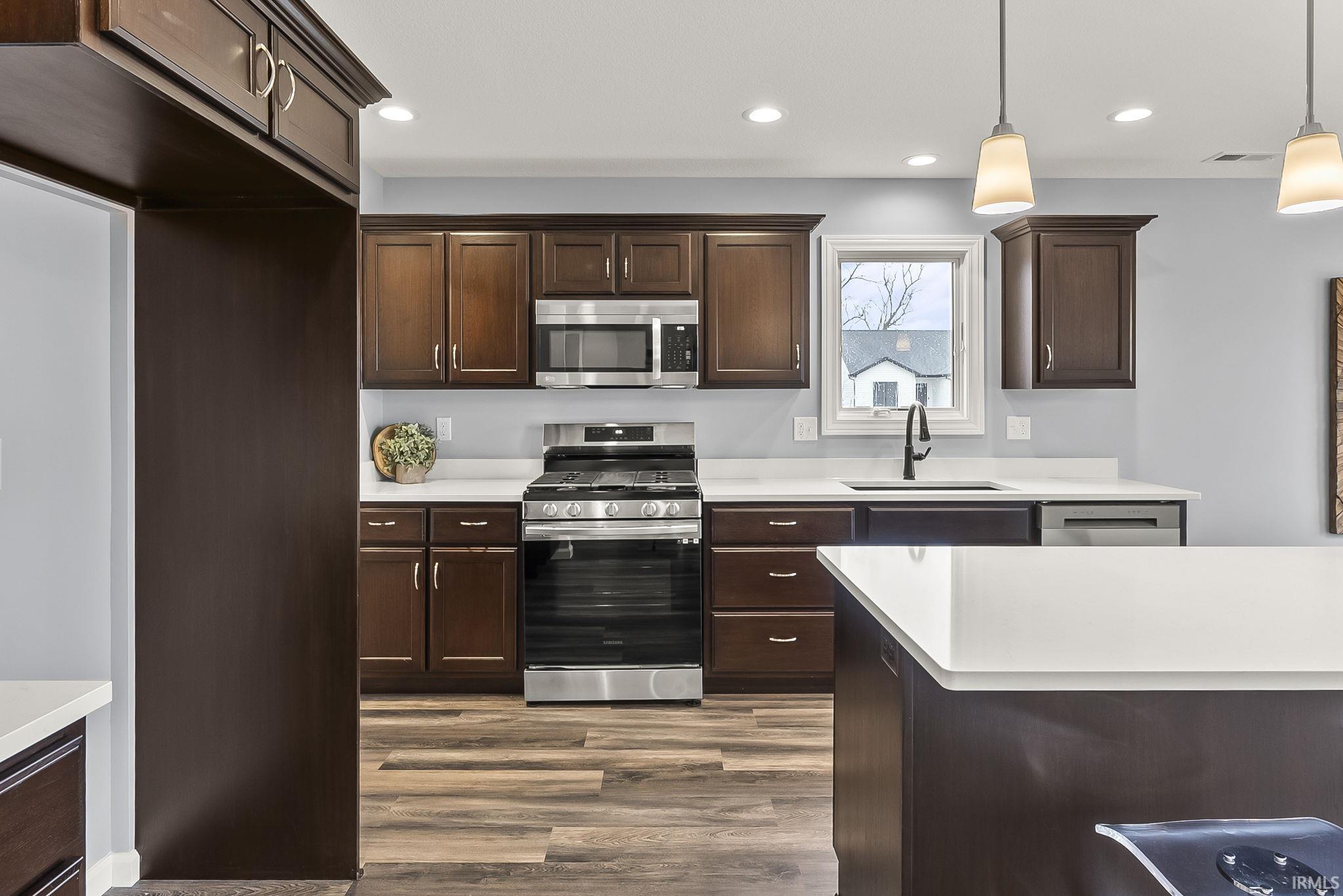 Kitchen featuring dark wood cabinetry, light countertops, stainless steel appliances, and wood-finish flooring