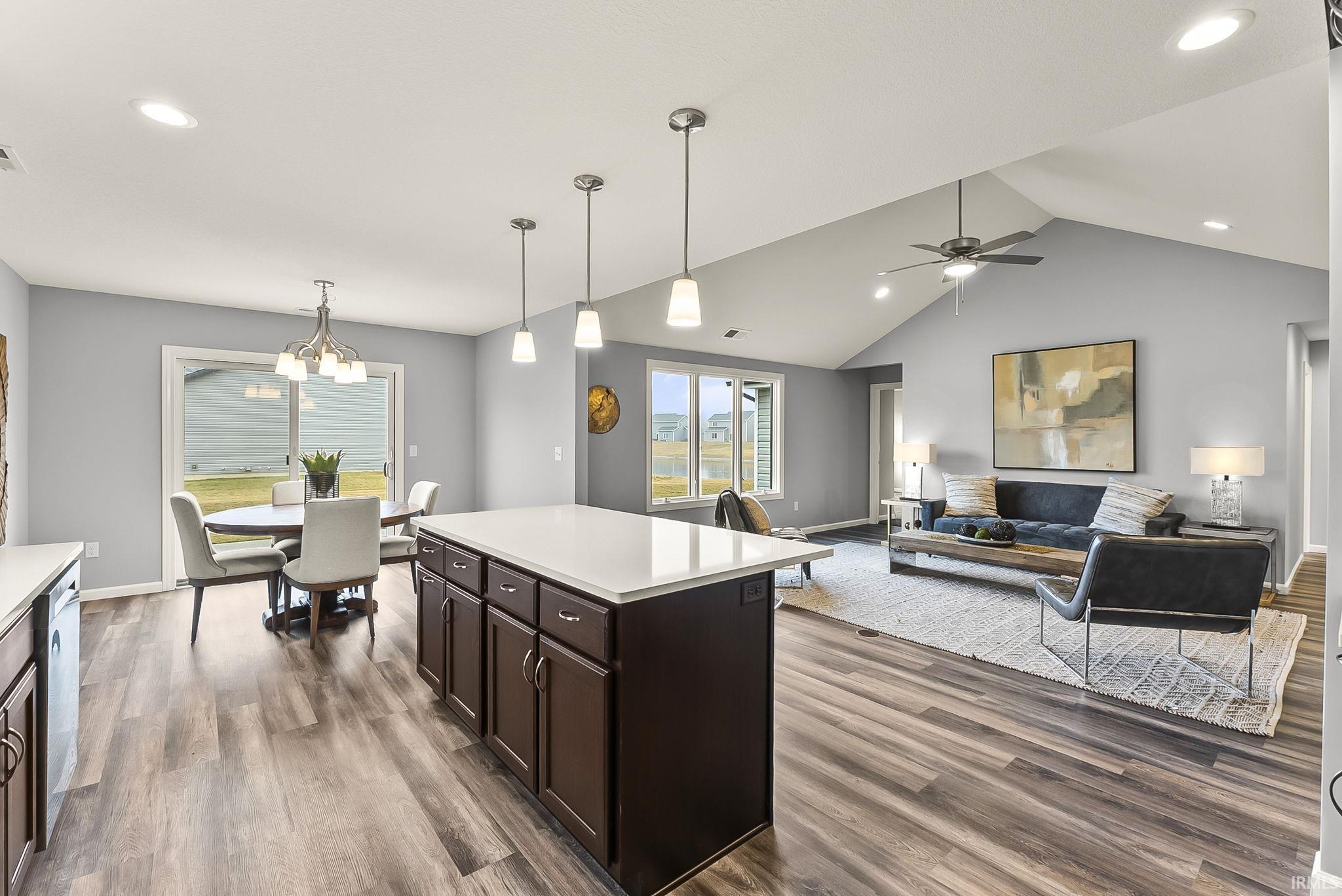 Spacious open-concept living area featuring a kitchen island with pendant lighting, wood-finish flooring, a vaulted ceiling, and sliding glass doors