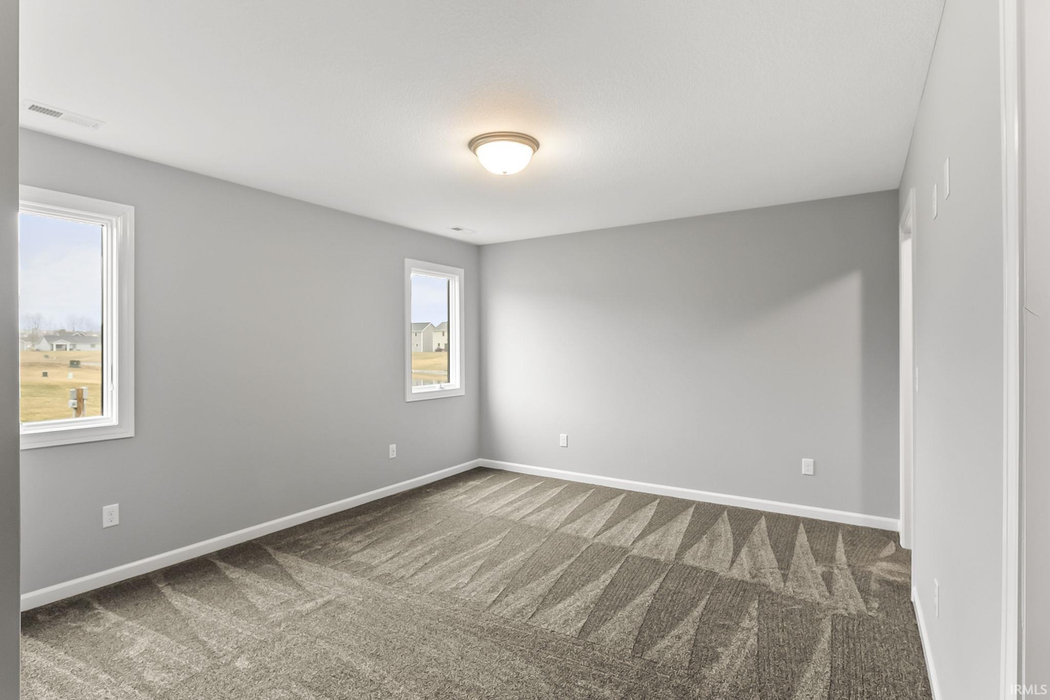 Carpeted room featuring a neutral color palette, two windows with white trim, a flush mount ceiling light fixture, and white baseboards