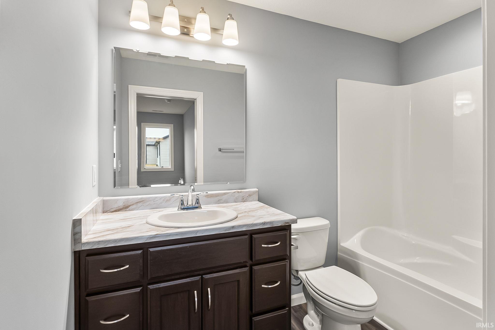 Bathroom featuring a dark wood vanity with a white oval sink, a marbled countertop, and a white integrated tub and shower unit