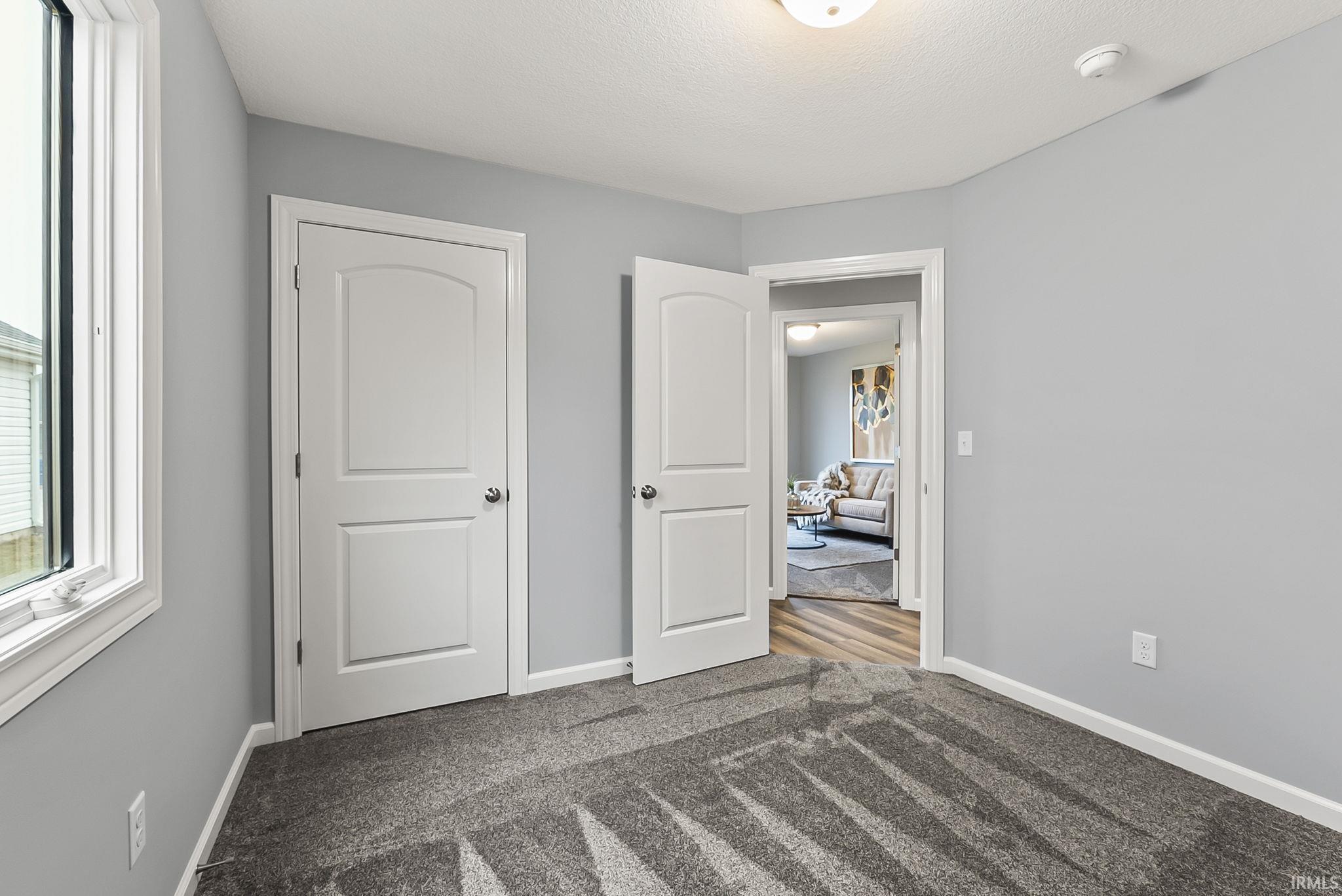 Interior room featuring light gray wall paint, white trim, gray patterned carpeting, and a white interior door