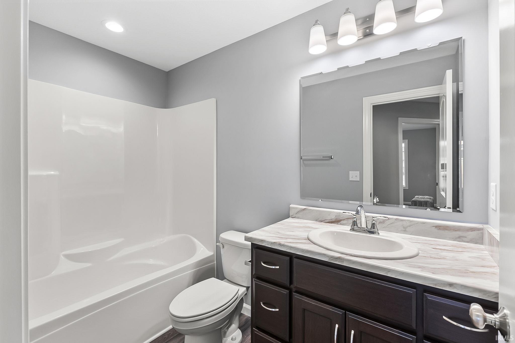 Bathroom featuring a white tub/shower combination, dark wood-finish vanity with a light-toned countertop, and a large wall-mounted mirror