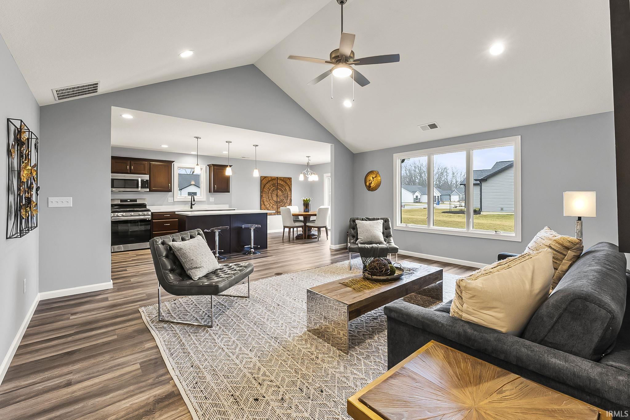 Vaulted ceiling living area featuring wood-finish flooring, a ceiling fan, and large windows