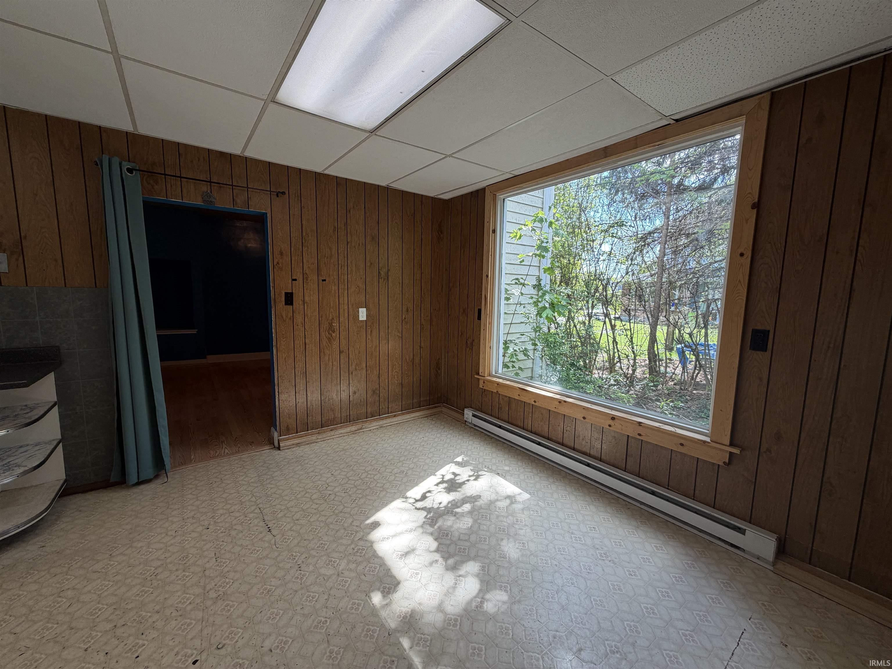 Room featuring wood-finish wall paneling, a large window with natural wood trim, and patterned vinyl flooring