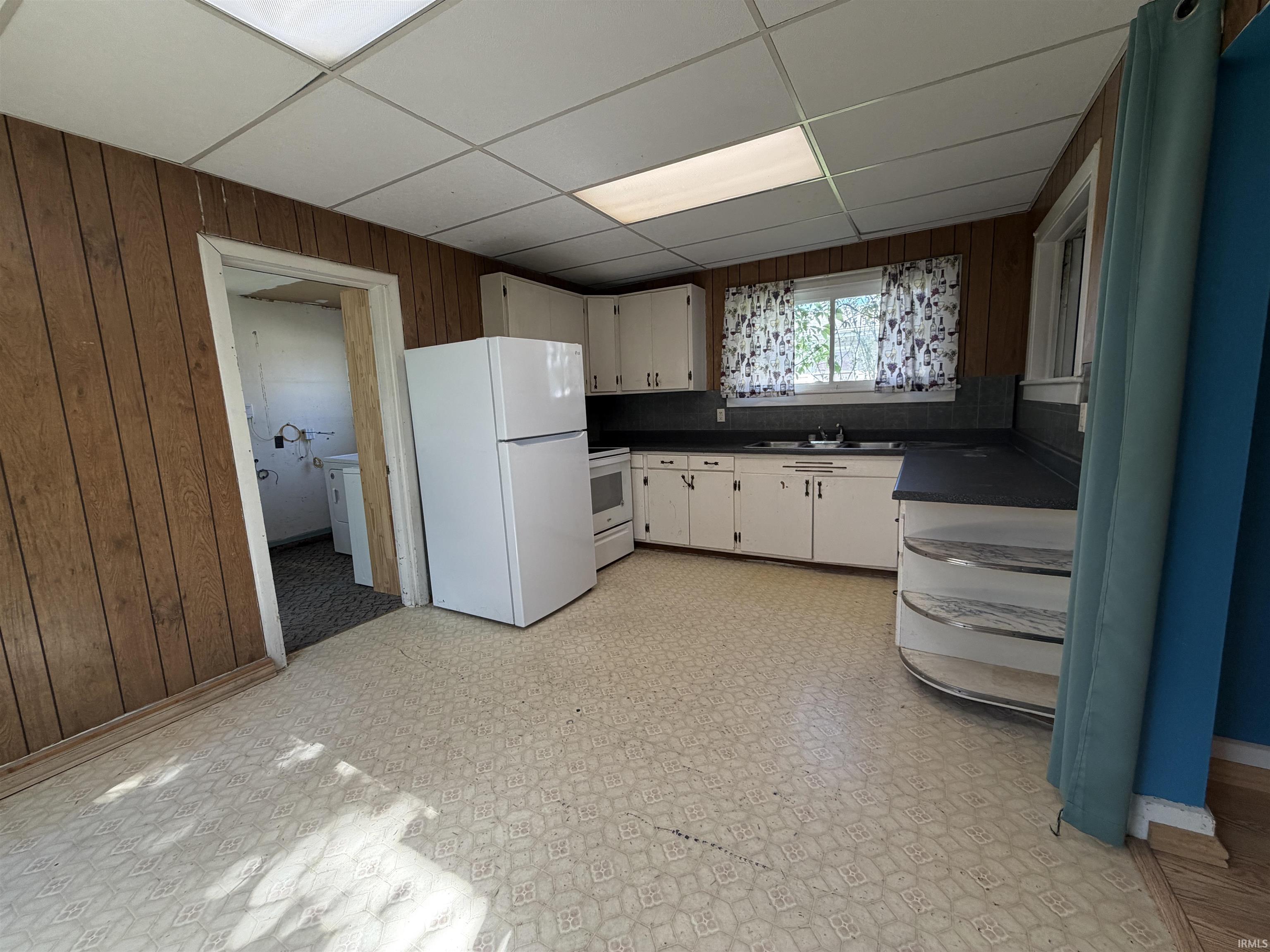 Kitchen featuring wood-panel walls, white cabinetry, dark countertops, and a drop-ceiling with recessed lighting