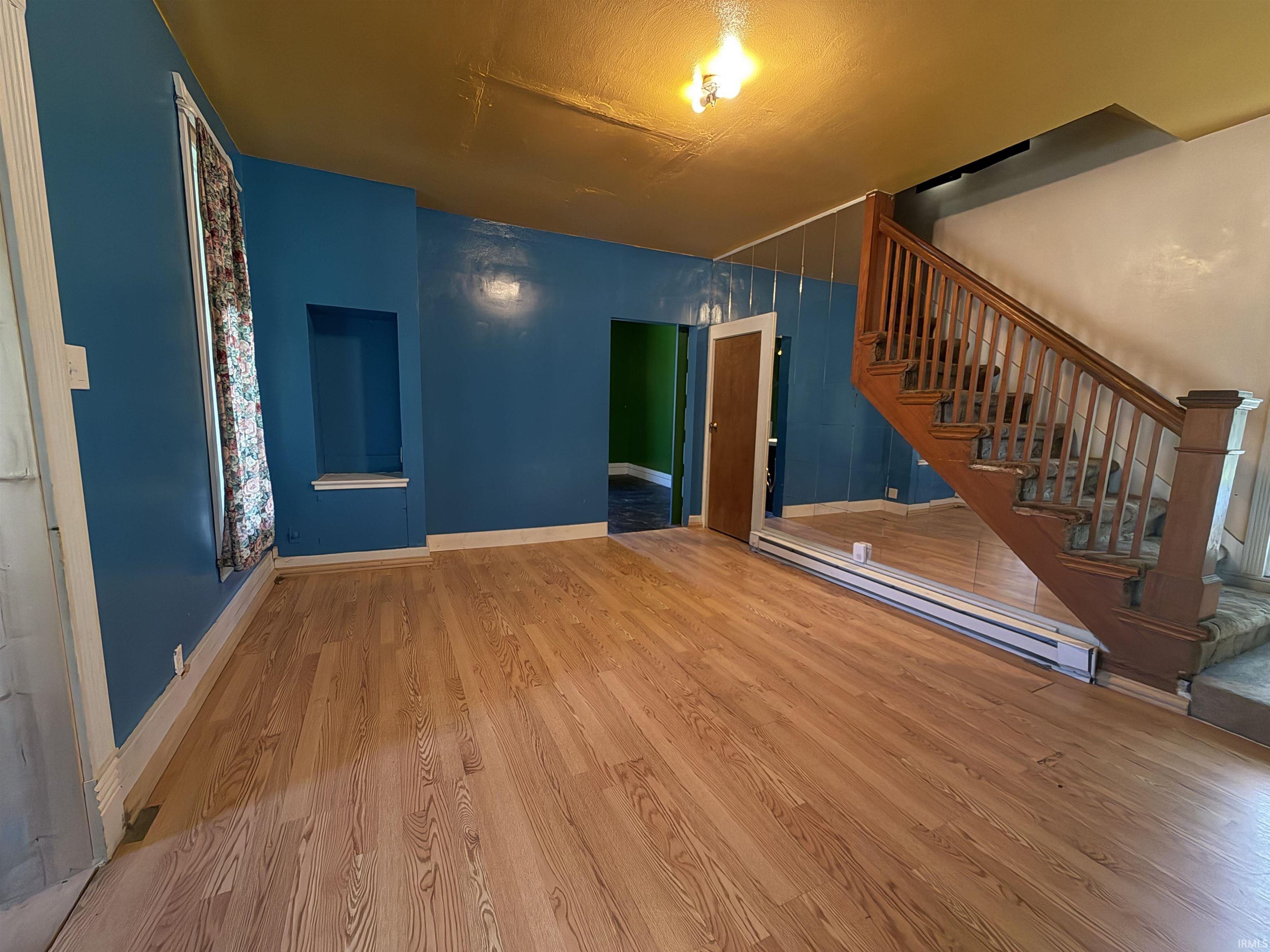 Spacious living area featuring wood-finish flooring, a traditional wooden staircase with banister, and a mirrored wall accent