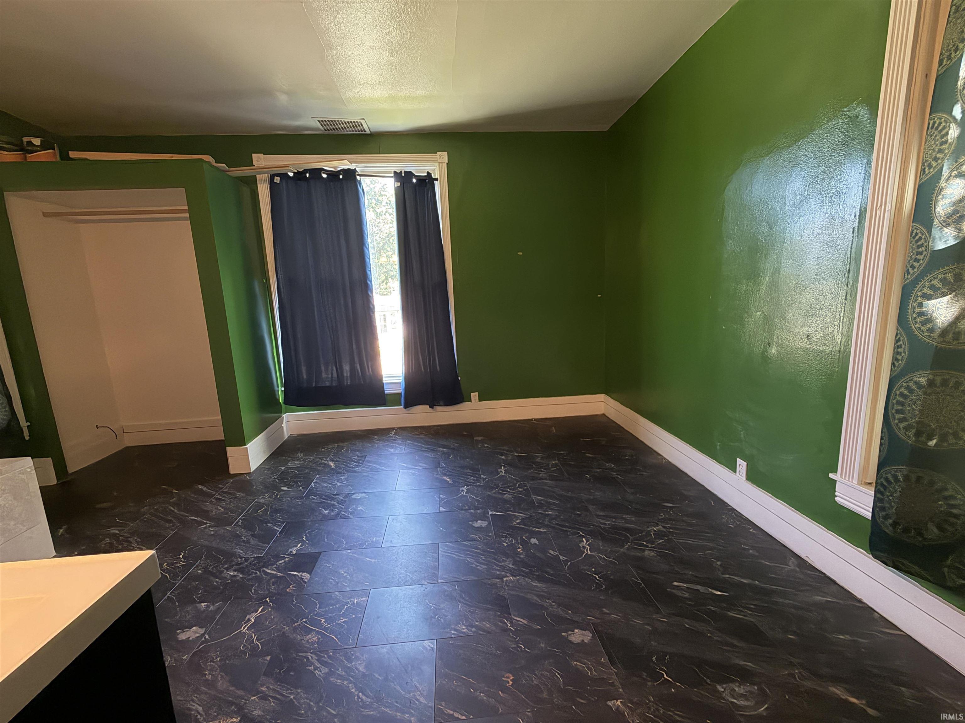Spacious room featuring patterned tile-look flooring, vibrant green walls, and white baseboards