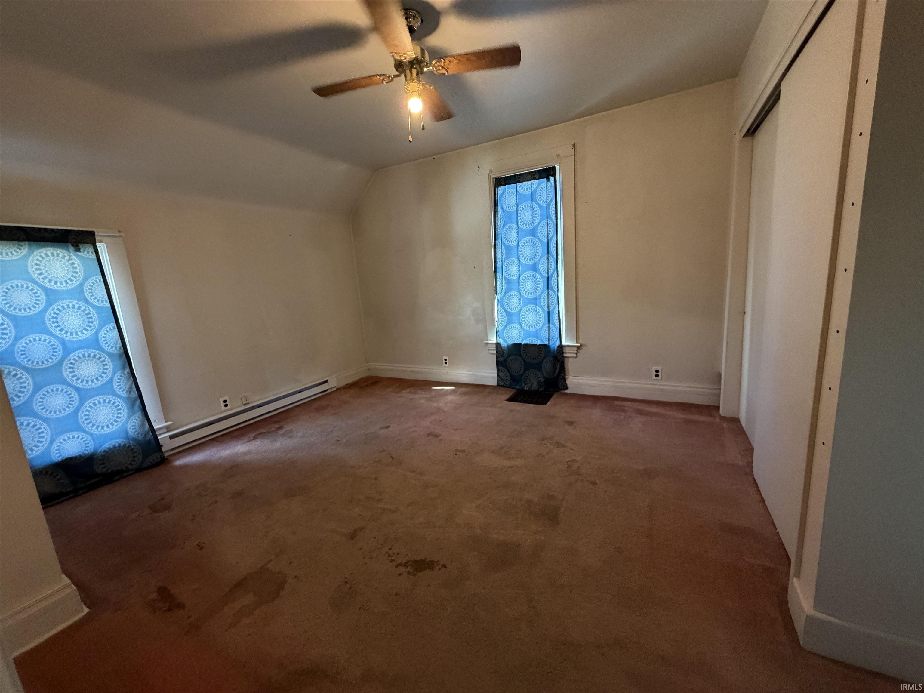 Room featuring an angled ceiling, two windows, and a ceiling fan with light fixture