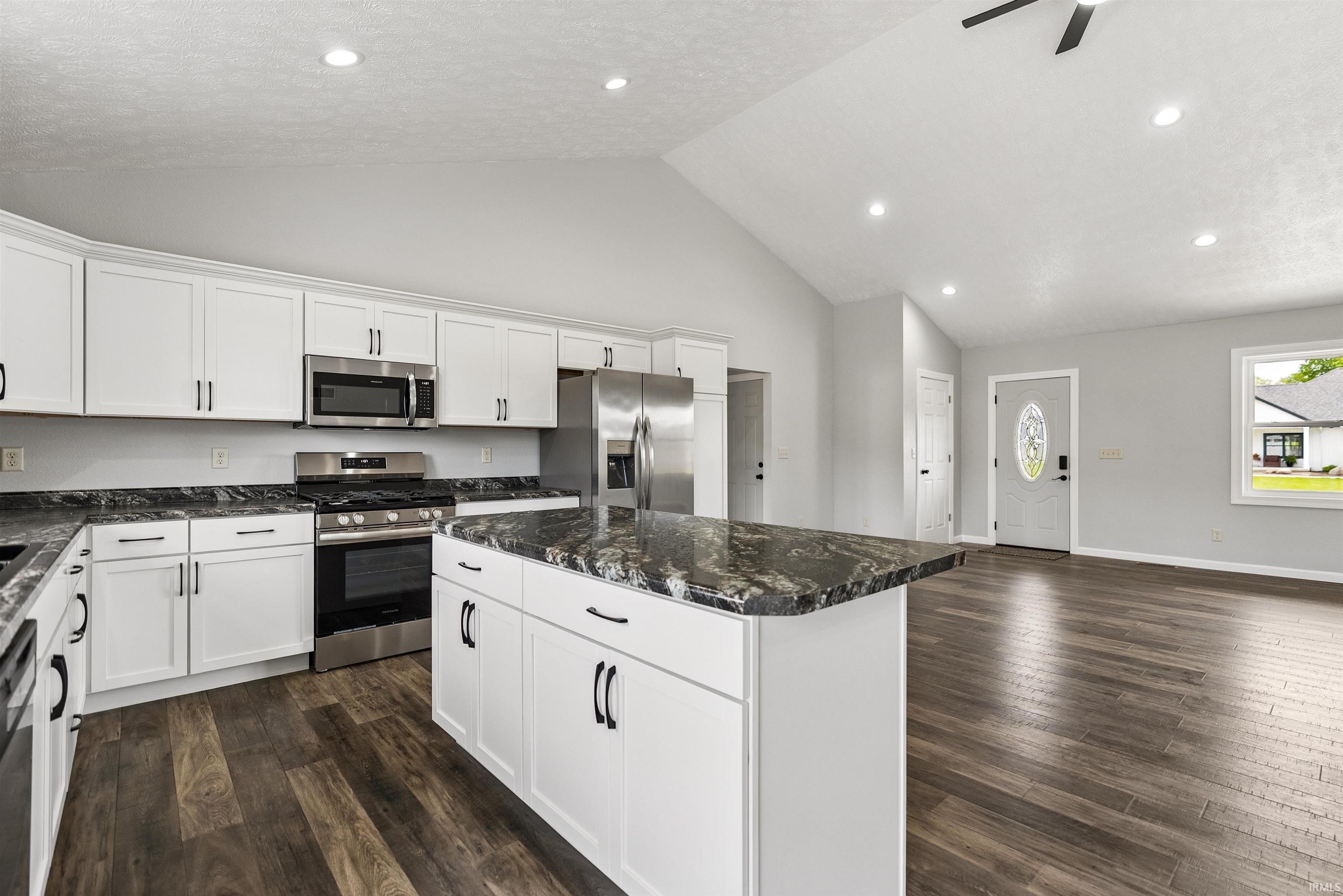 Open-concept kitchen featuring white cabinetry, dark stone countertops, and stainless steel appliances