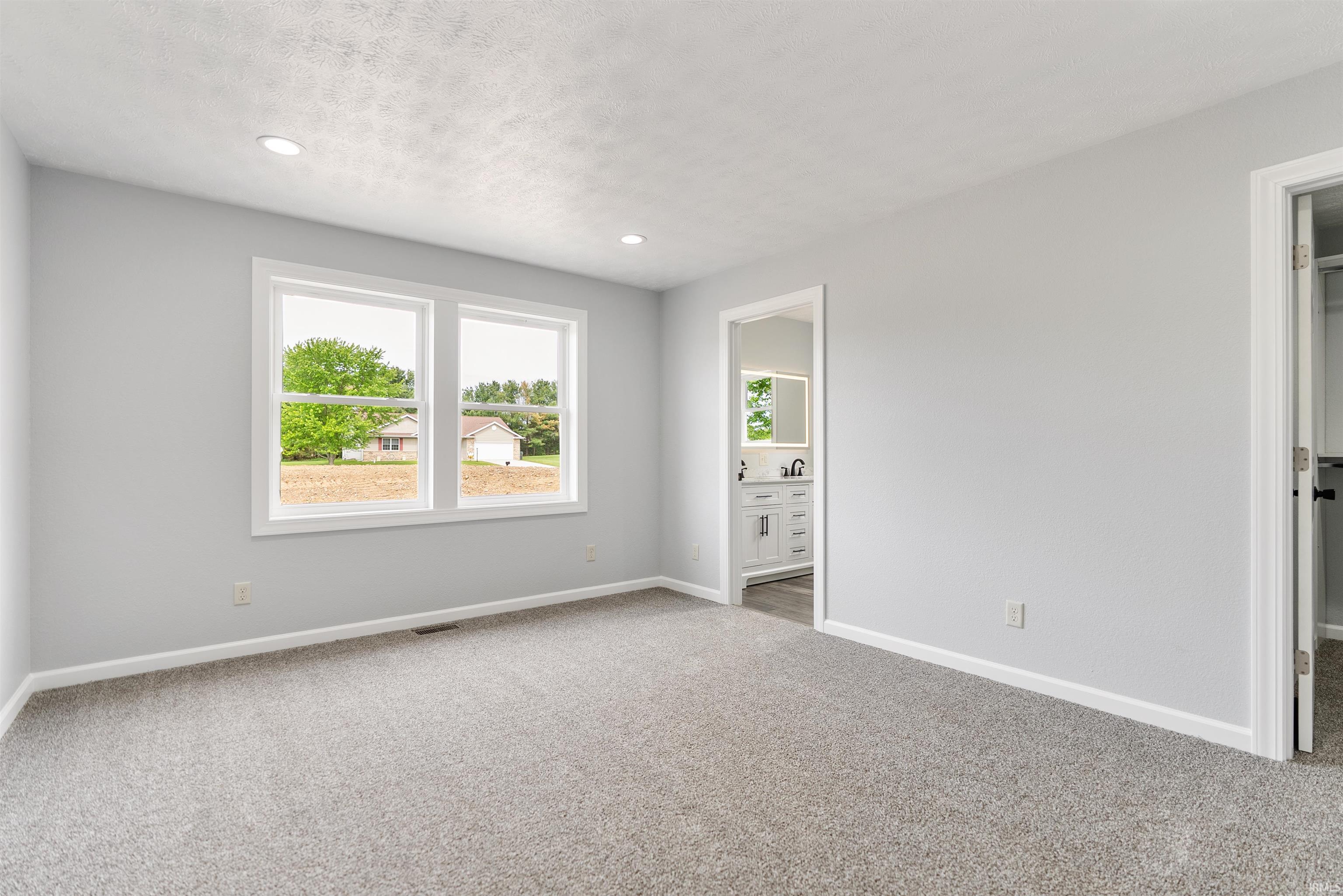 Spacious room featuring light gray carpeting, recessed lighting, and a white trim package