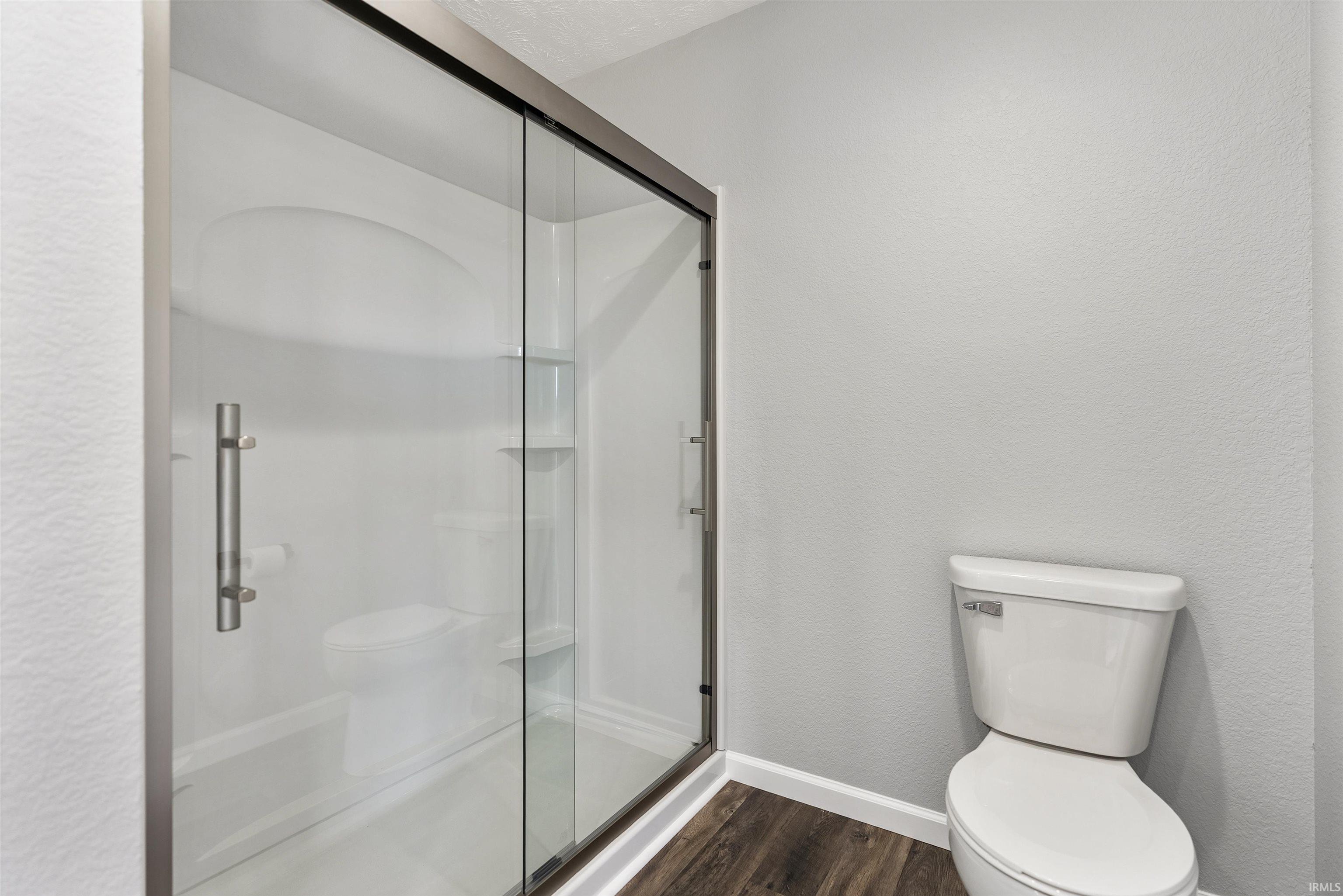 Glass-enclosed shower with a white surround and built-in shelving, accompanied by a white toilet