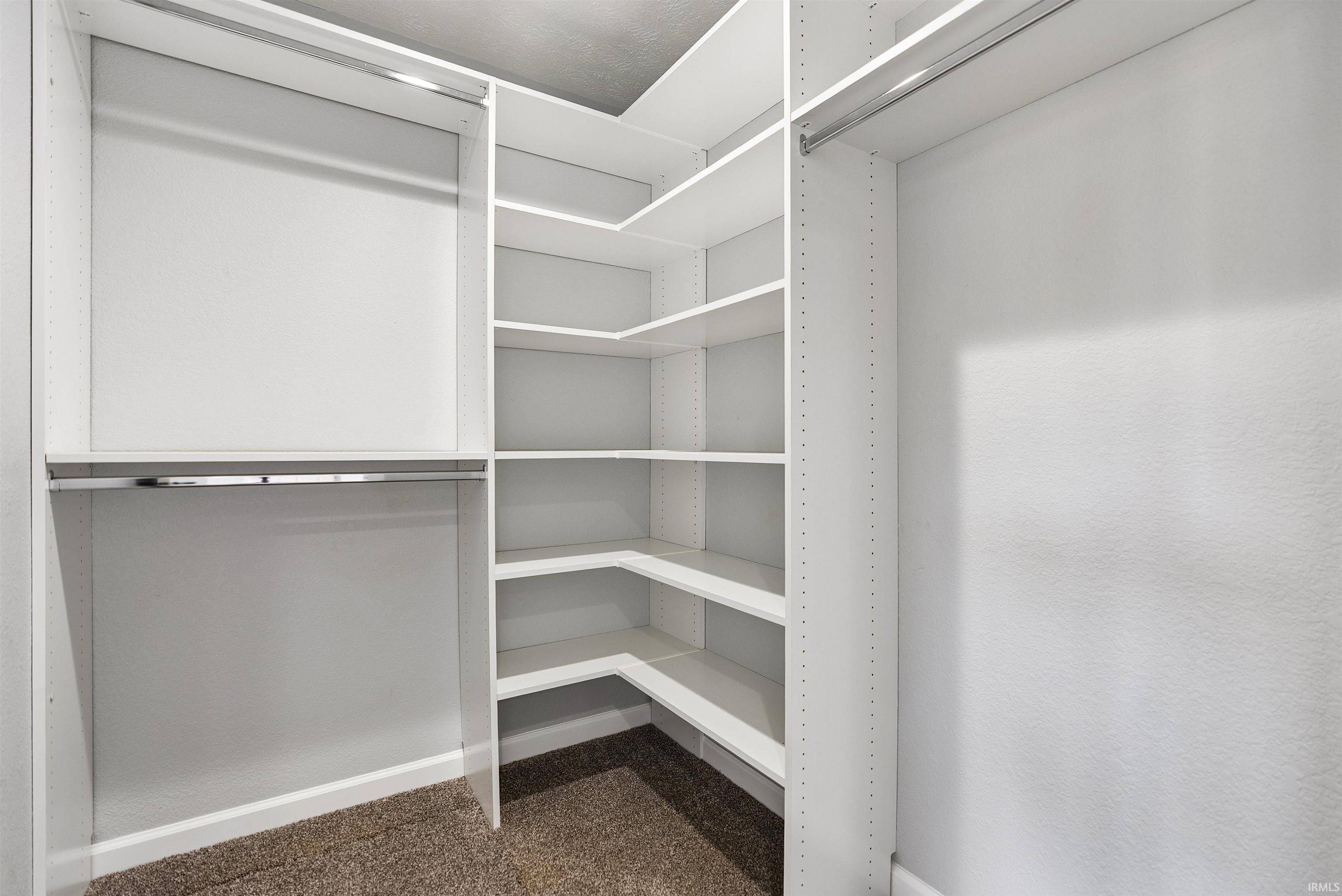 Walk-in closet featuring white built-in shelving, multiple hanging rods, and a neutral carpeted floor
