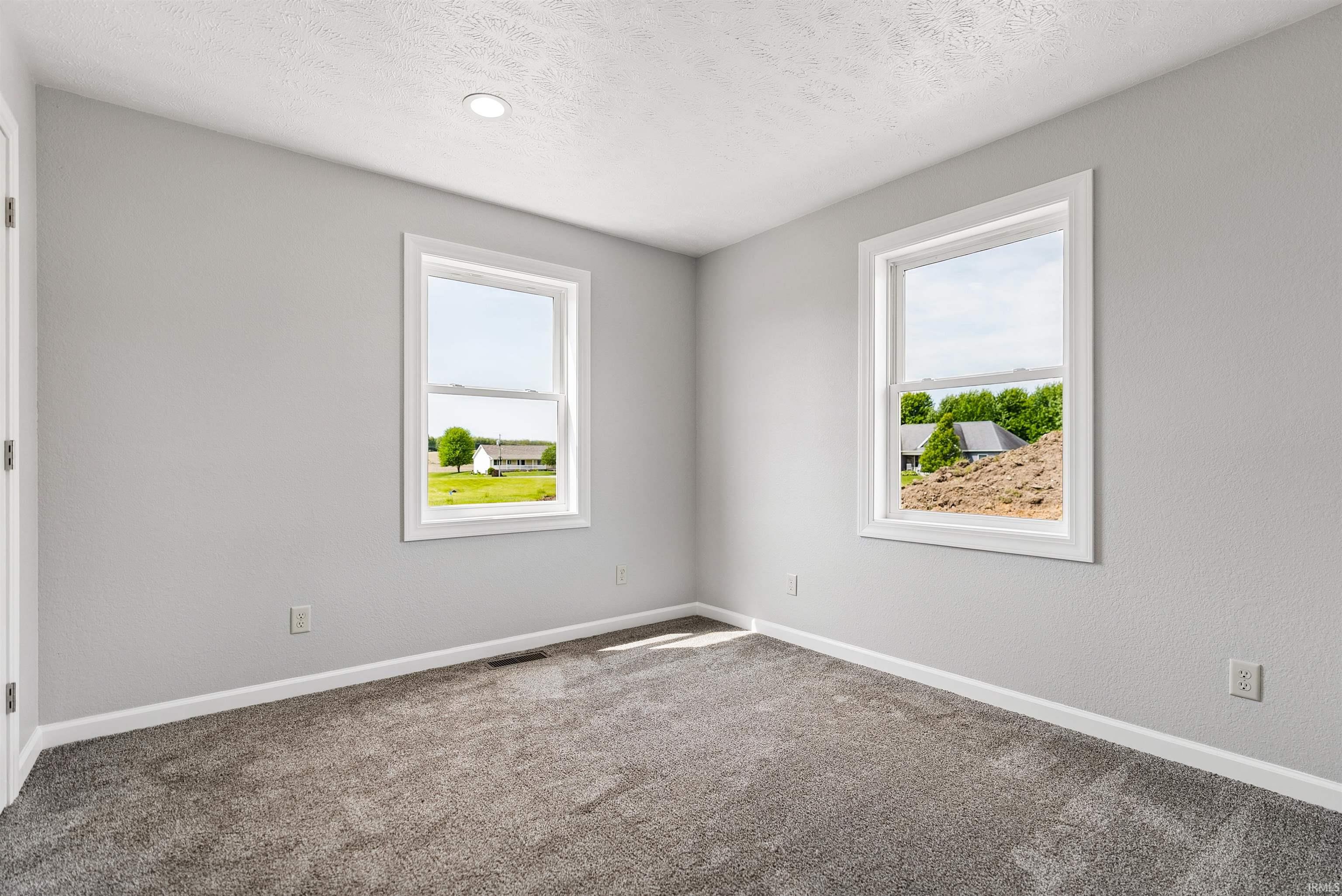 Neutral-toned interior room featuring two windows with white trim, recessed ceiling lighting, and gray textured carpeting