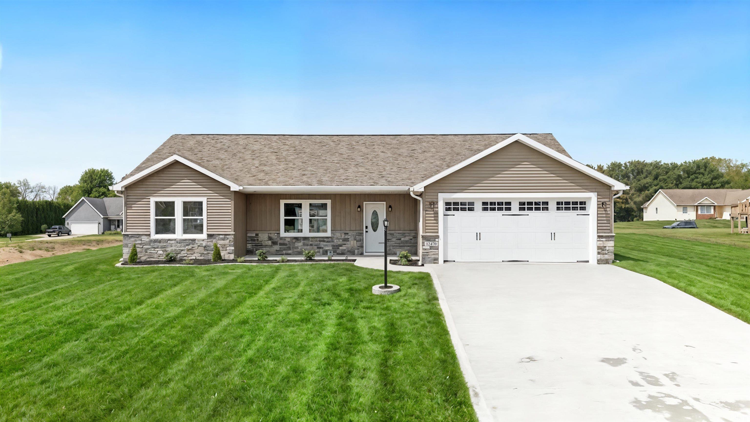 Ranch-style residence featuring a tan siding exterior with stone veneer accents, a white garage door, and a concrete driveway