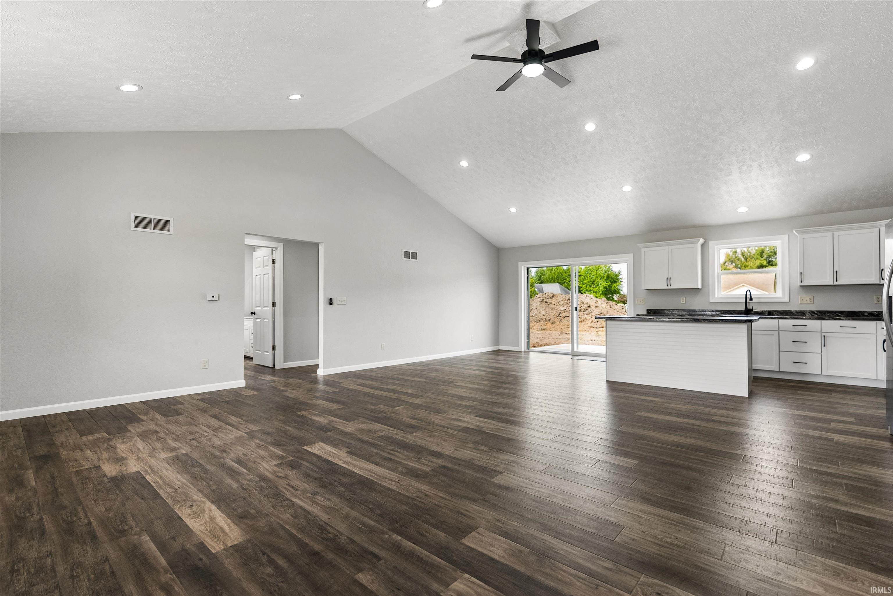 Open-concept living space featuring wood-finish flooring, vaulted ceilings, recessed lighting, and a modern ceiling fan