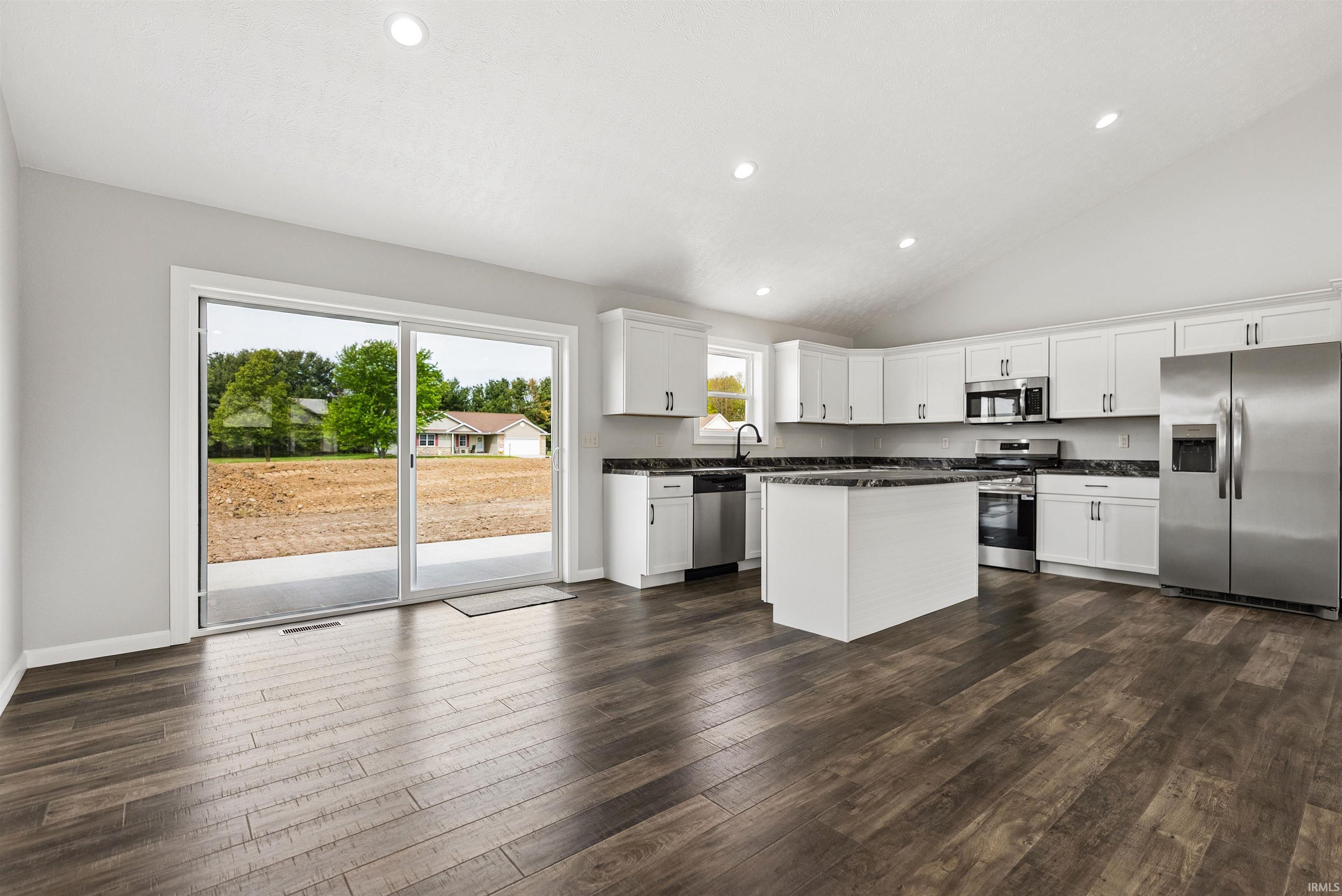 Modern kitchen featuring white cabinetry, stainless steel appliances, dark countertops, and wood-finish flooring