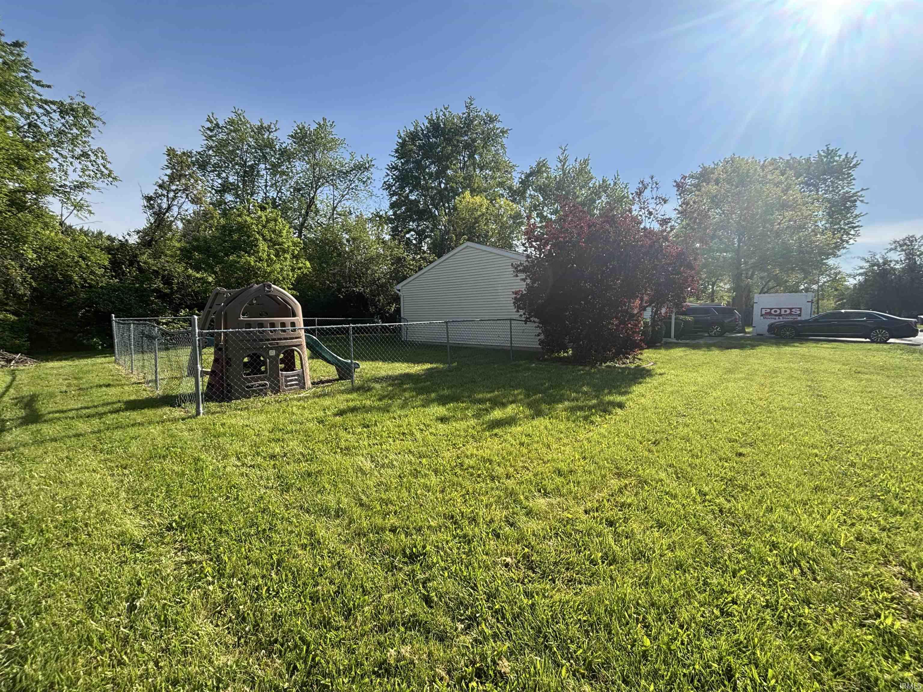Expansive grassy yard area featuring a chain-link fence, mature trees, and a detached structure with light-colored siding