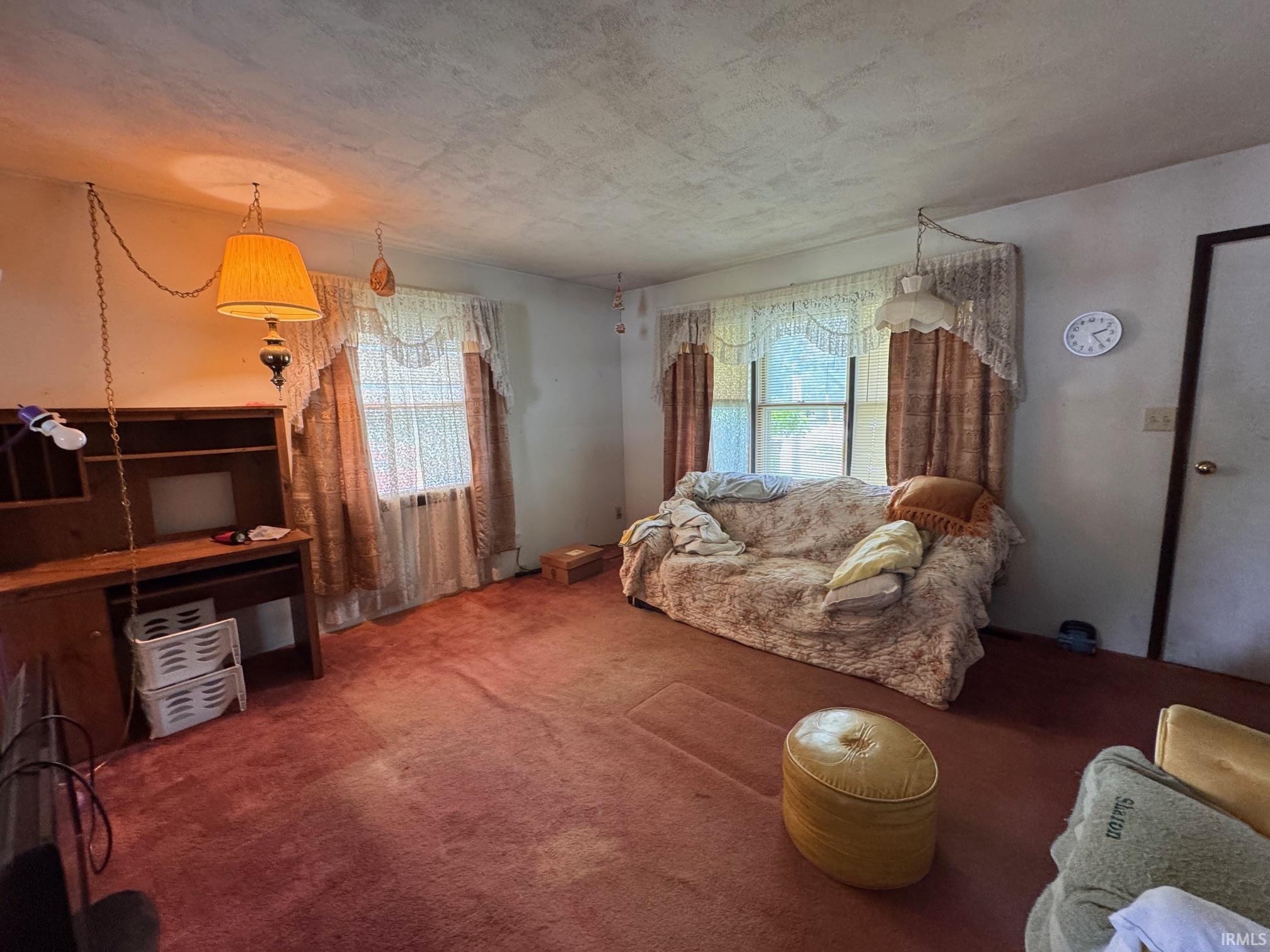 Carpeted interior space featuring two windows, a built-in wooden desk unit, and a suspended lighting fixture