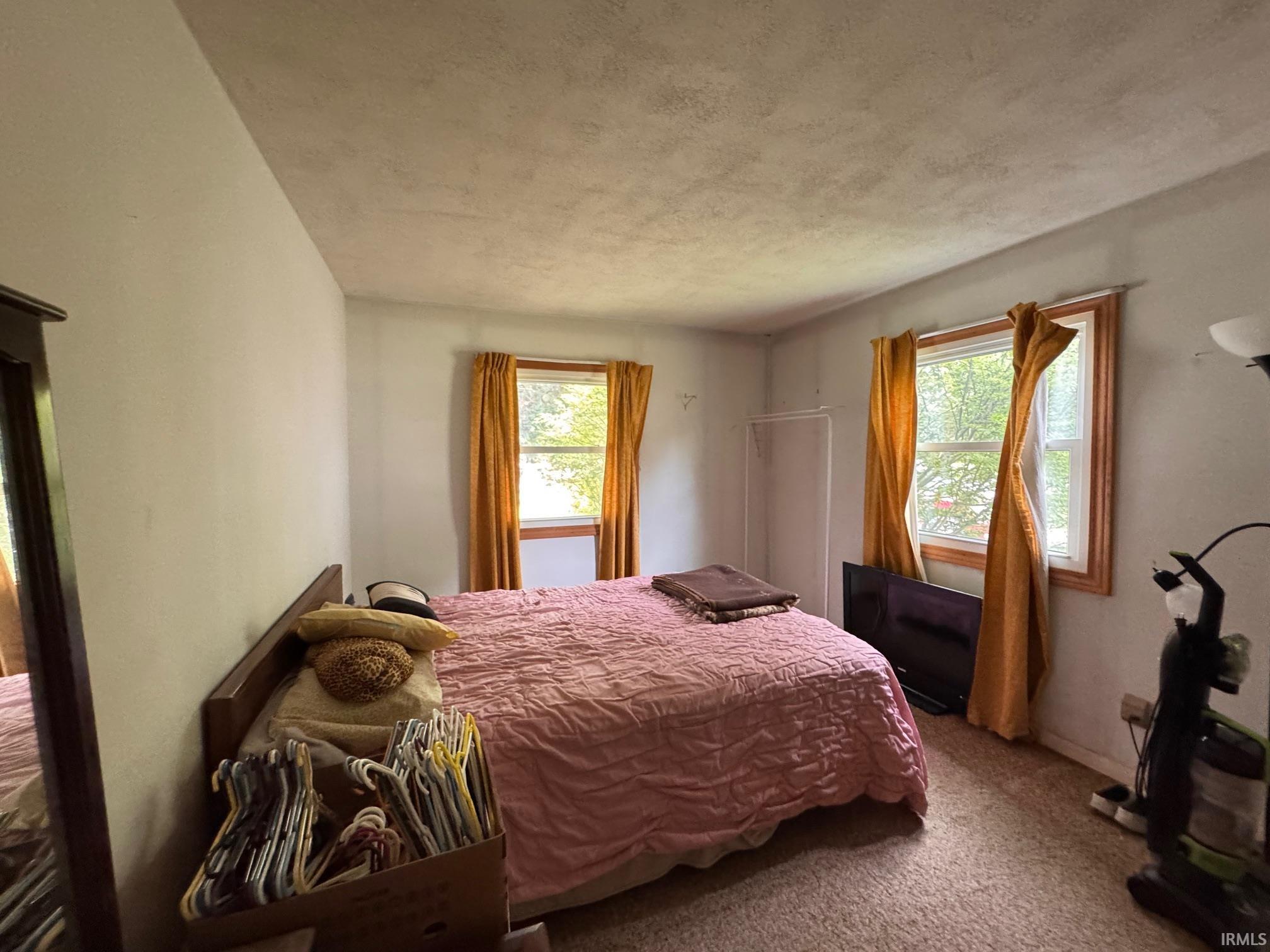 Bedroom featuring two windows with wood trim, light-colored walls, and textured ceiling