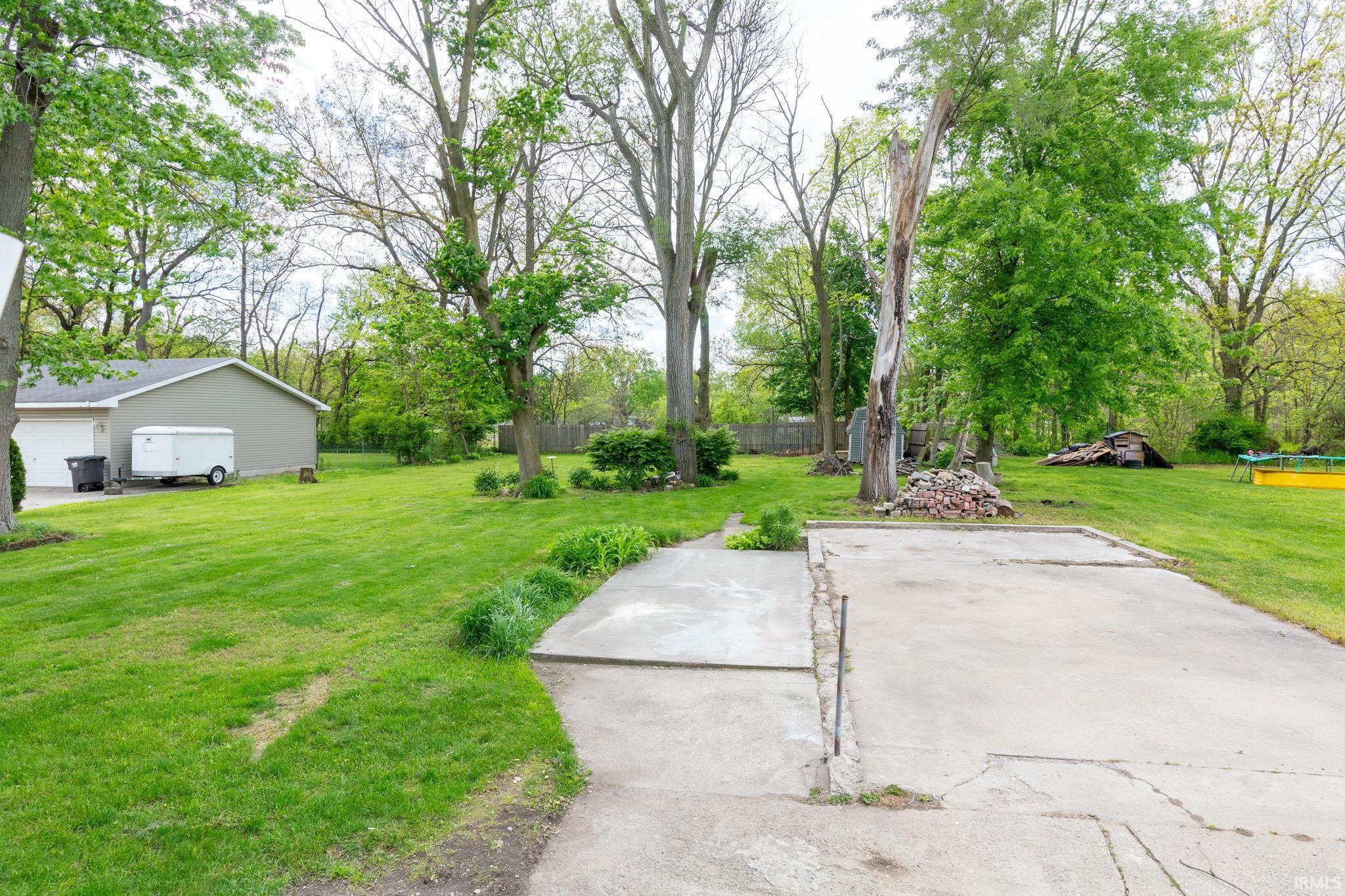 Expansive yard featuring concrete pad, mature trees, and a detached garage with two overhead doors
