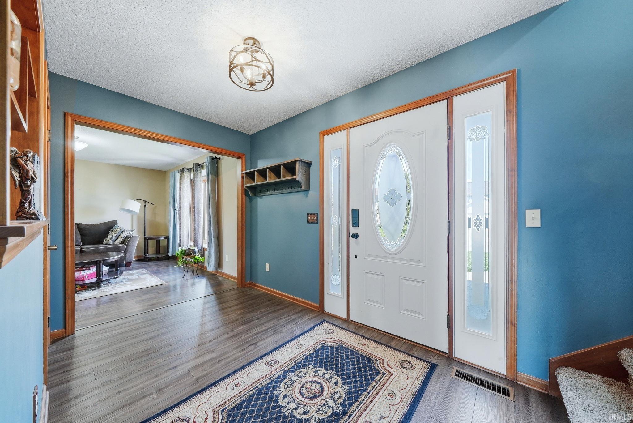 Foyer with wood-finish flooring, a white entry door with decorative glass, and coordinating sidelight panels