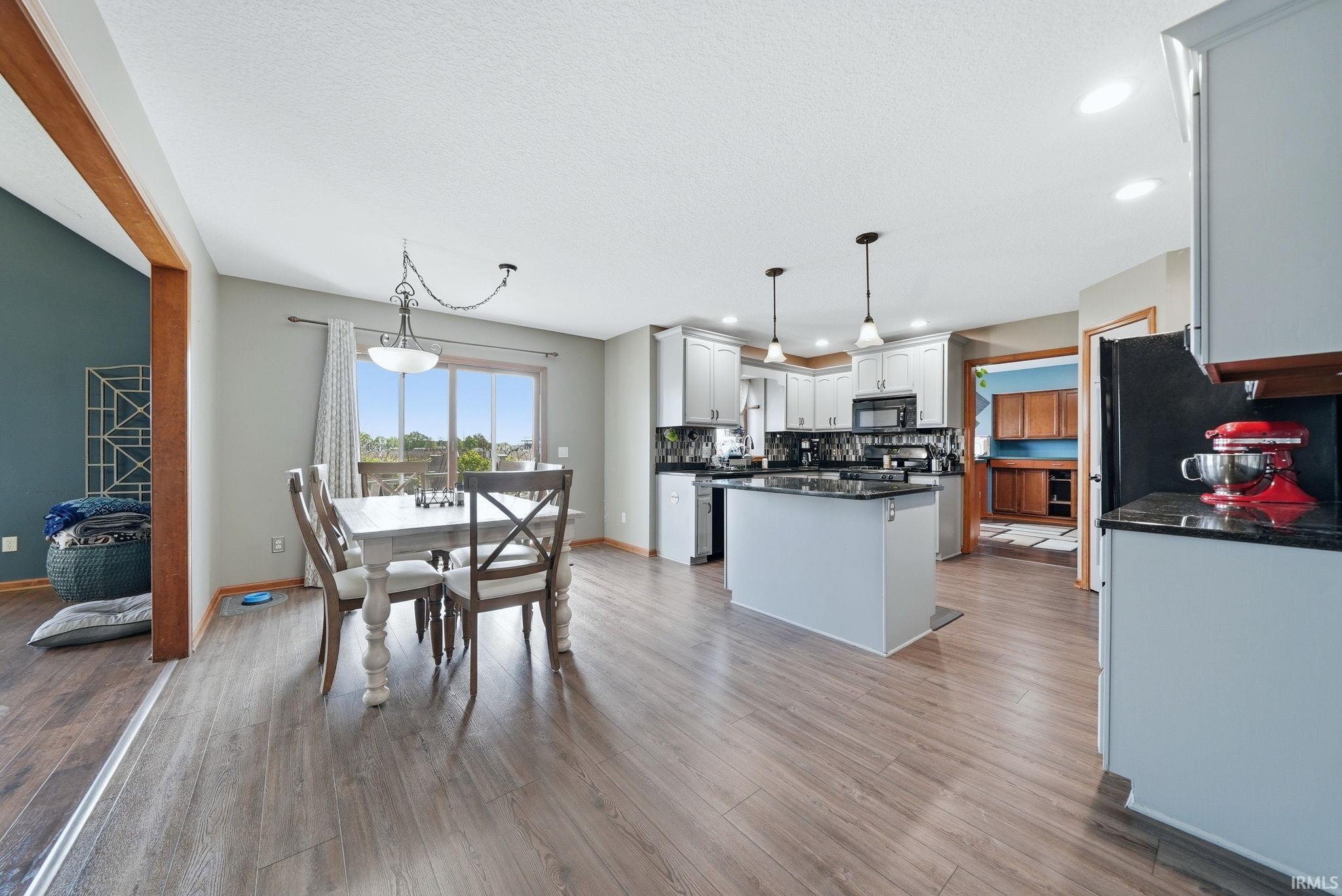 Open-concept dining area and kitchen featuring wood-finish flooring, white cabinetry, dark countertops, and stainless steel appliances