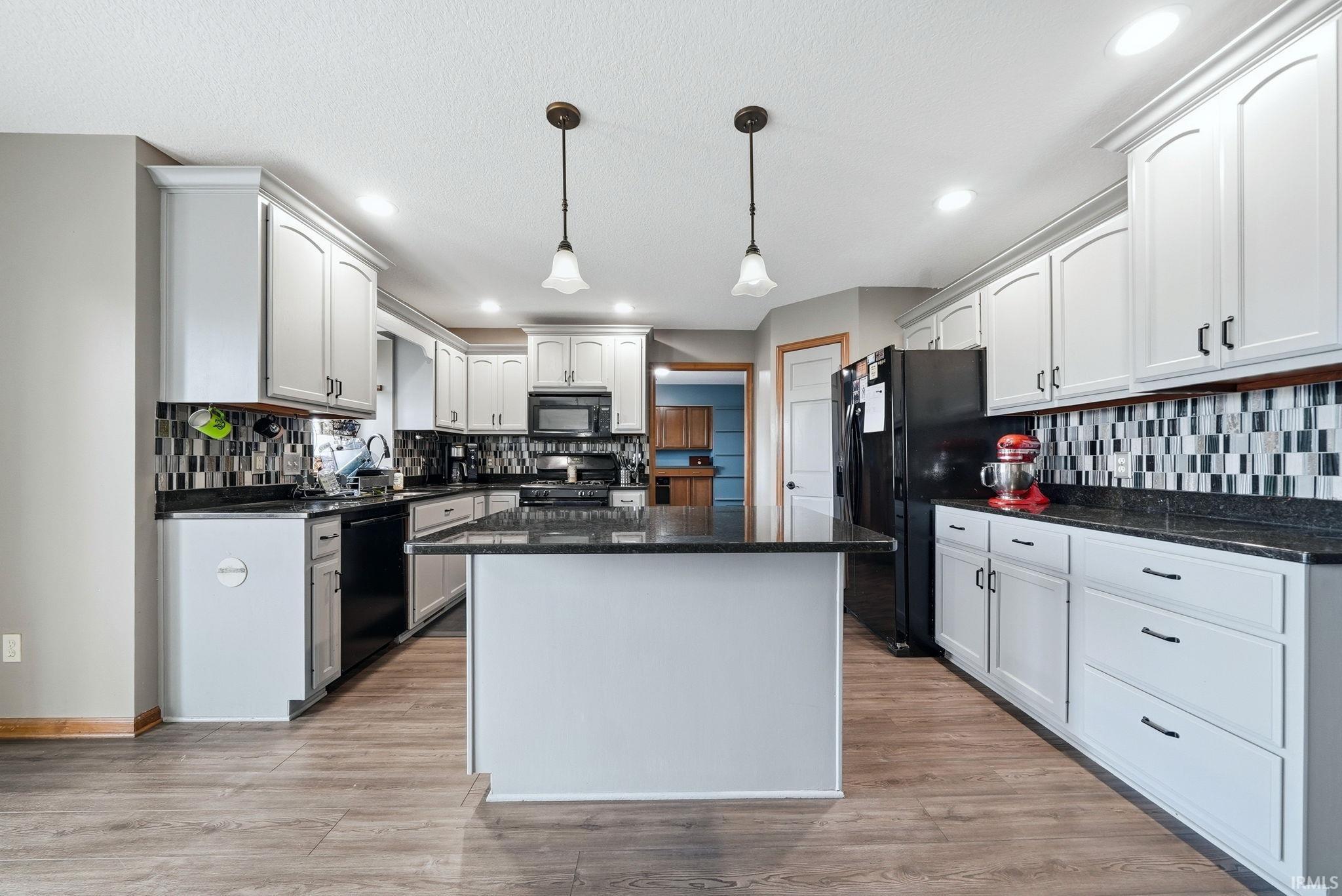 Spacious kitchen featuring an island, black countertops, a mosaic tile backsplash, wood-finish flooring, and recessed lighting