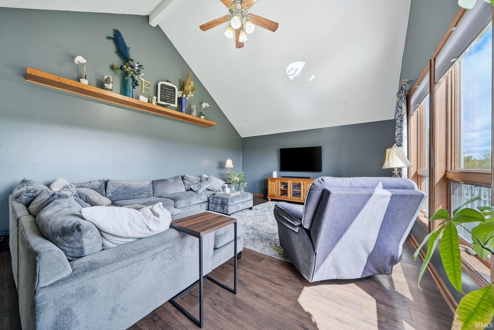 Vaulted ceiling with a wood-finish ceiling fan, expansive window bank with wood-finish framing, wood-finish flooring, and a built-in wall shelf