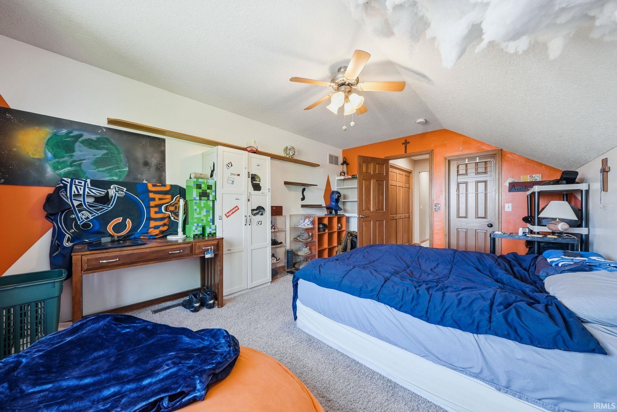 Carpeted room featuring a ceiling fan with light fixture, white storage cabinetry, and an angled ceiling line