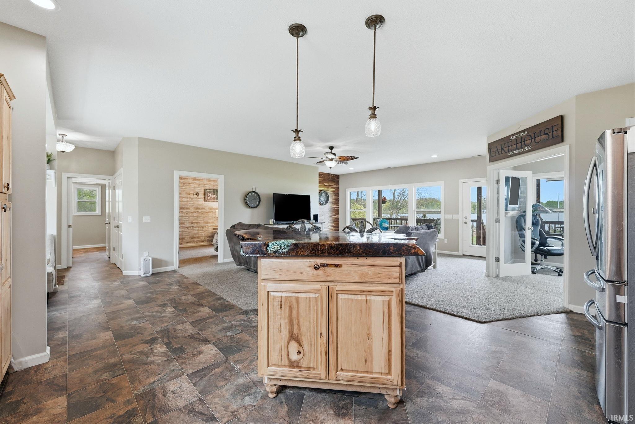 Open-concept living area featuring a kitchen island with a live-edge countertop, pendant lighting, wood-finish flooring, and multiple windows offering expansive water views