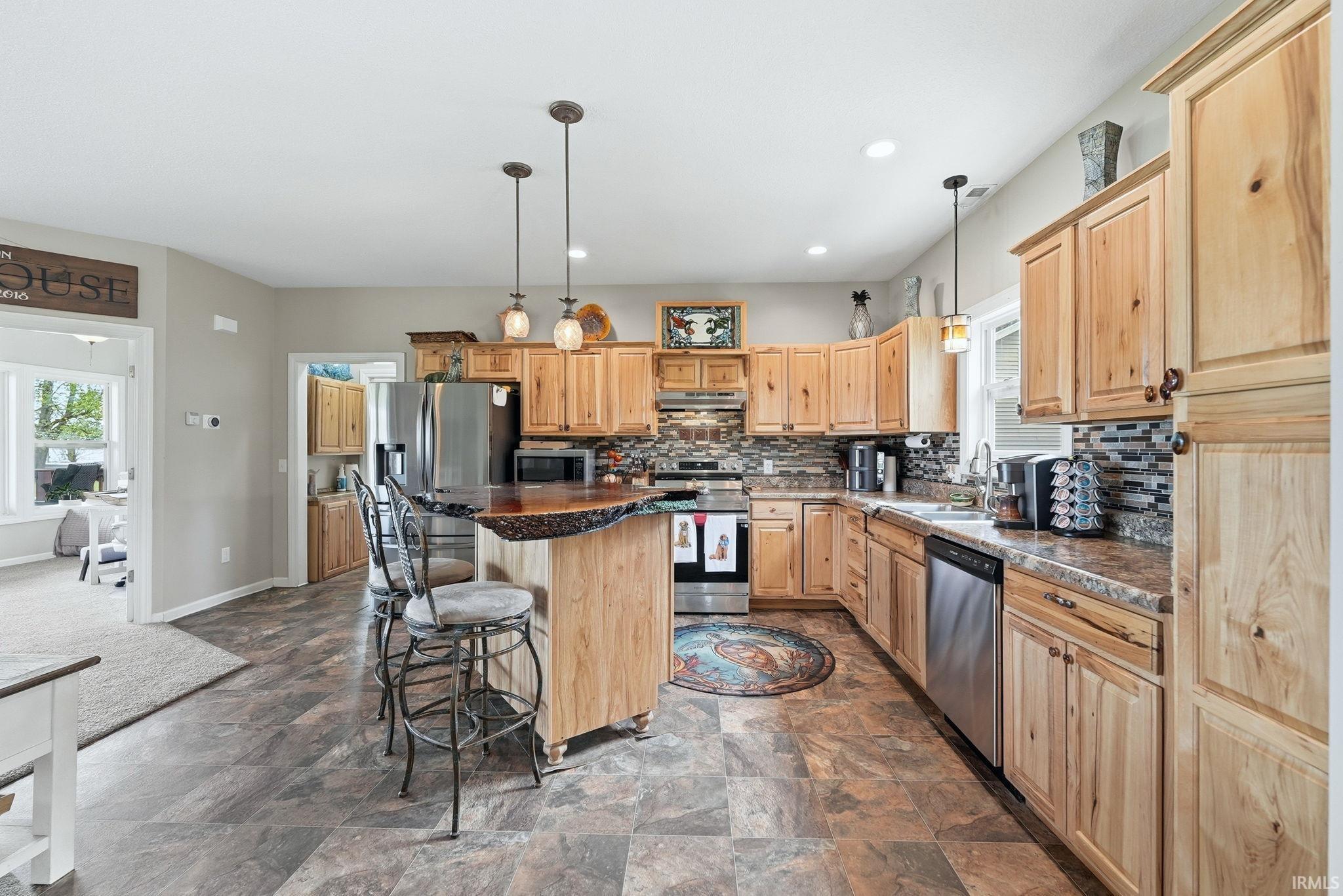Spacious kitchen featuring natural wood cabinetry, stainless steel appliances, a mosaic tile backsplash, and an island with pendant lighting