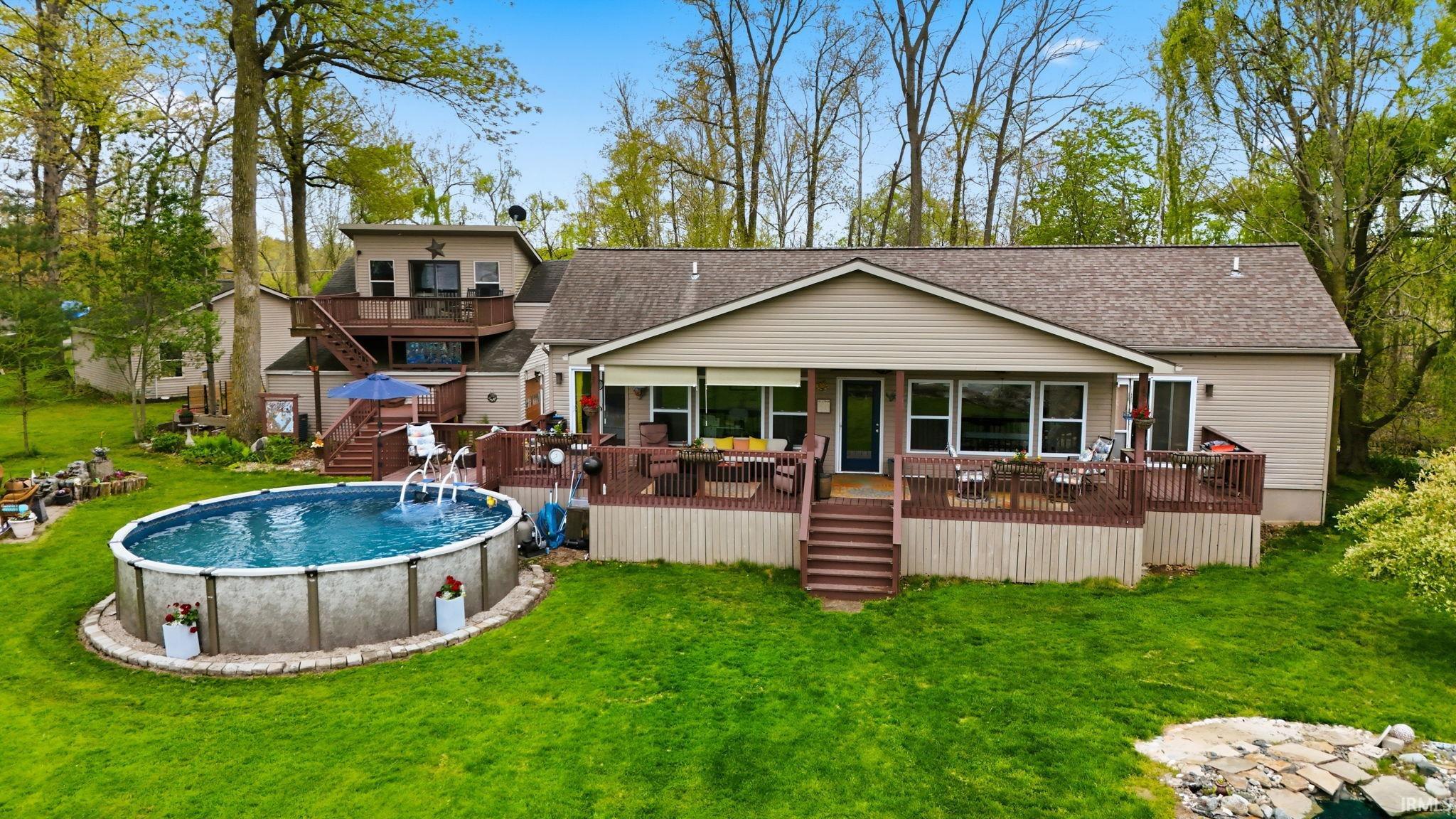 Expansive backyard featuring a large above-ground swimming pool, a multi-level wood deck, and a multi-level residence with siding exterior