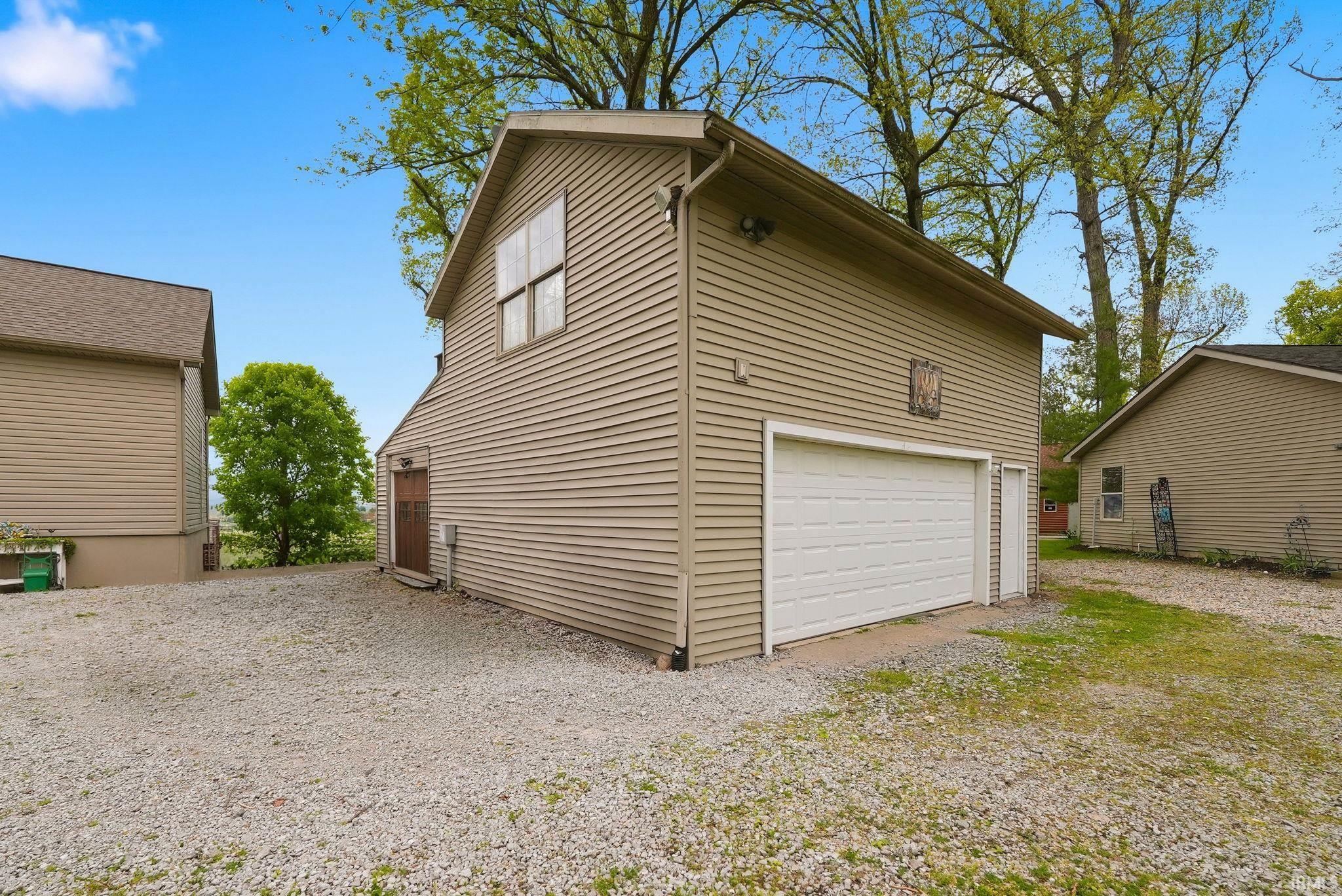 Two-story detached garage featuring tan horizontal siding, a white overhead garage door, a side entry door, and an upper-level window
