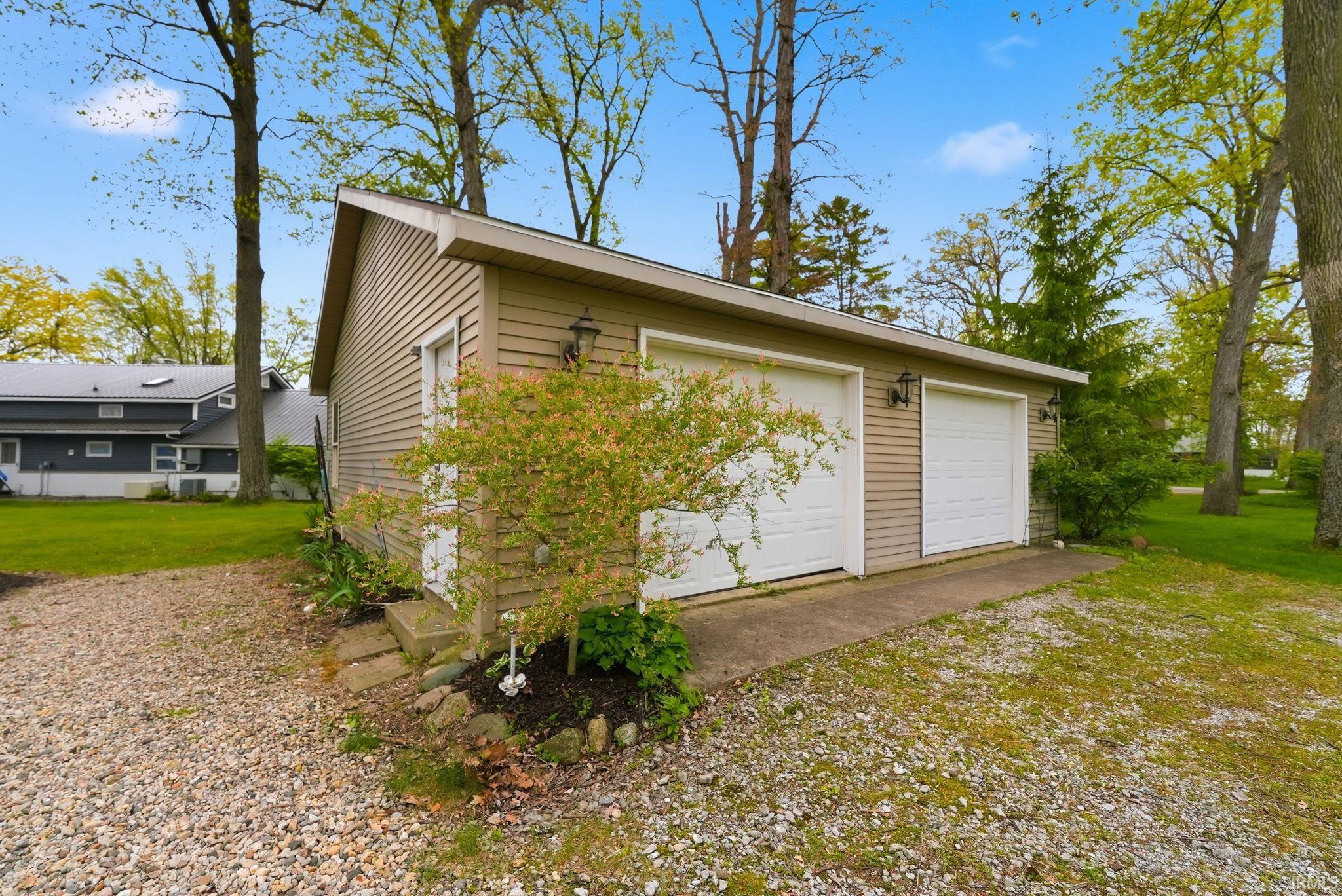 Detached two-car garage featuring tan siding, two white roll-up garage doors, and a side access door