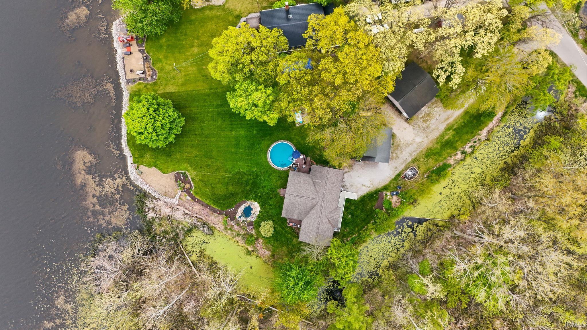 Waterfront property featuring a circular swimming pool, expansive green lawn, mature trees, and a detached structure