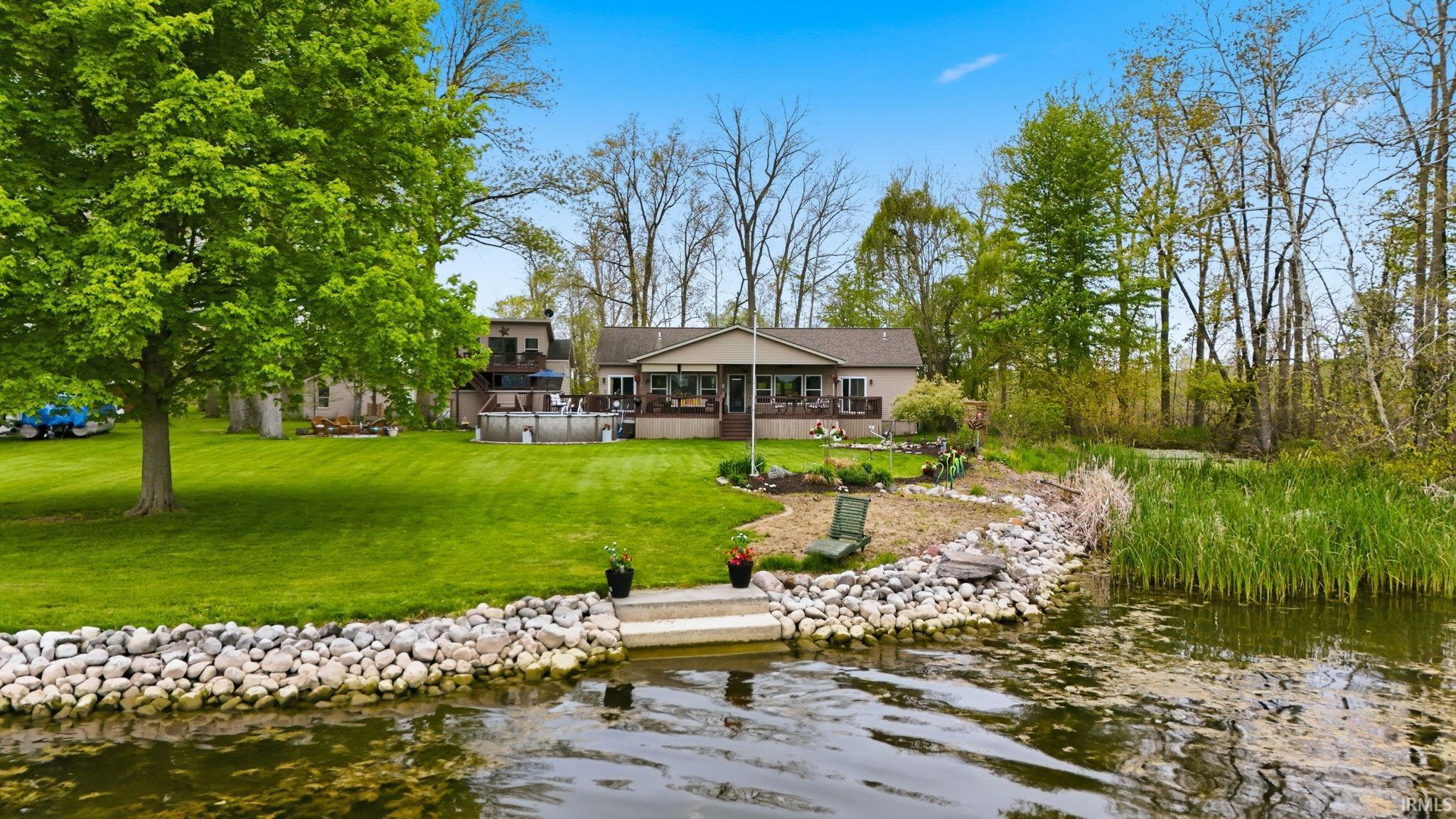 Expansive waterfront property featuring a manicured lawn, mature trees, and a multi-level deck