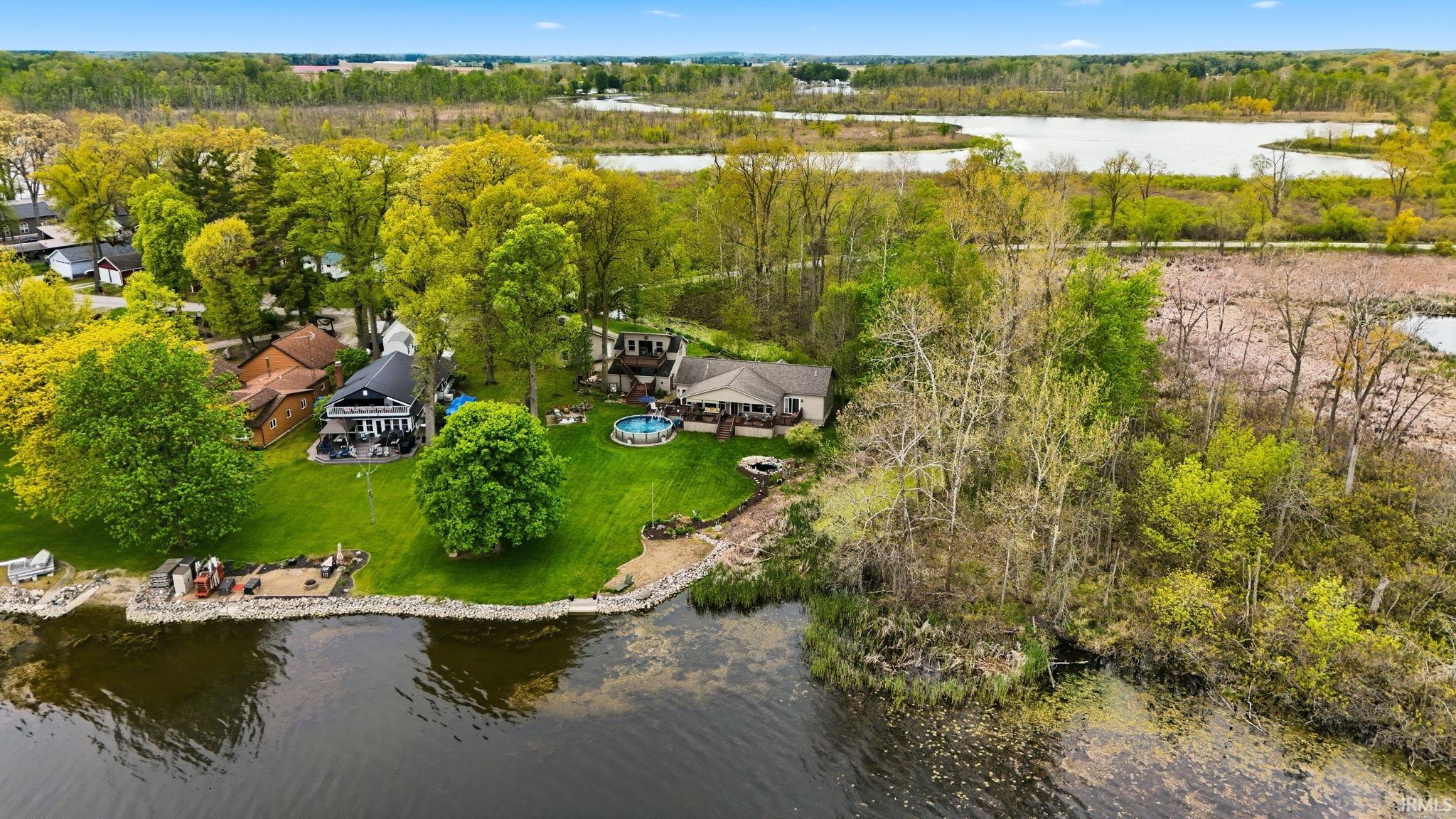 Waterfront property featuring a private boat launch, expansive green lawn, mature trees, an outdoor swimming pool, and a fire pit area