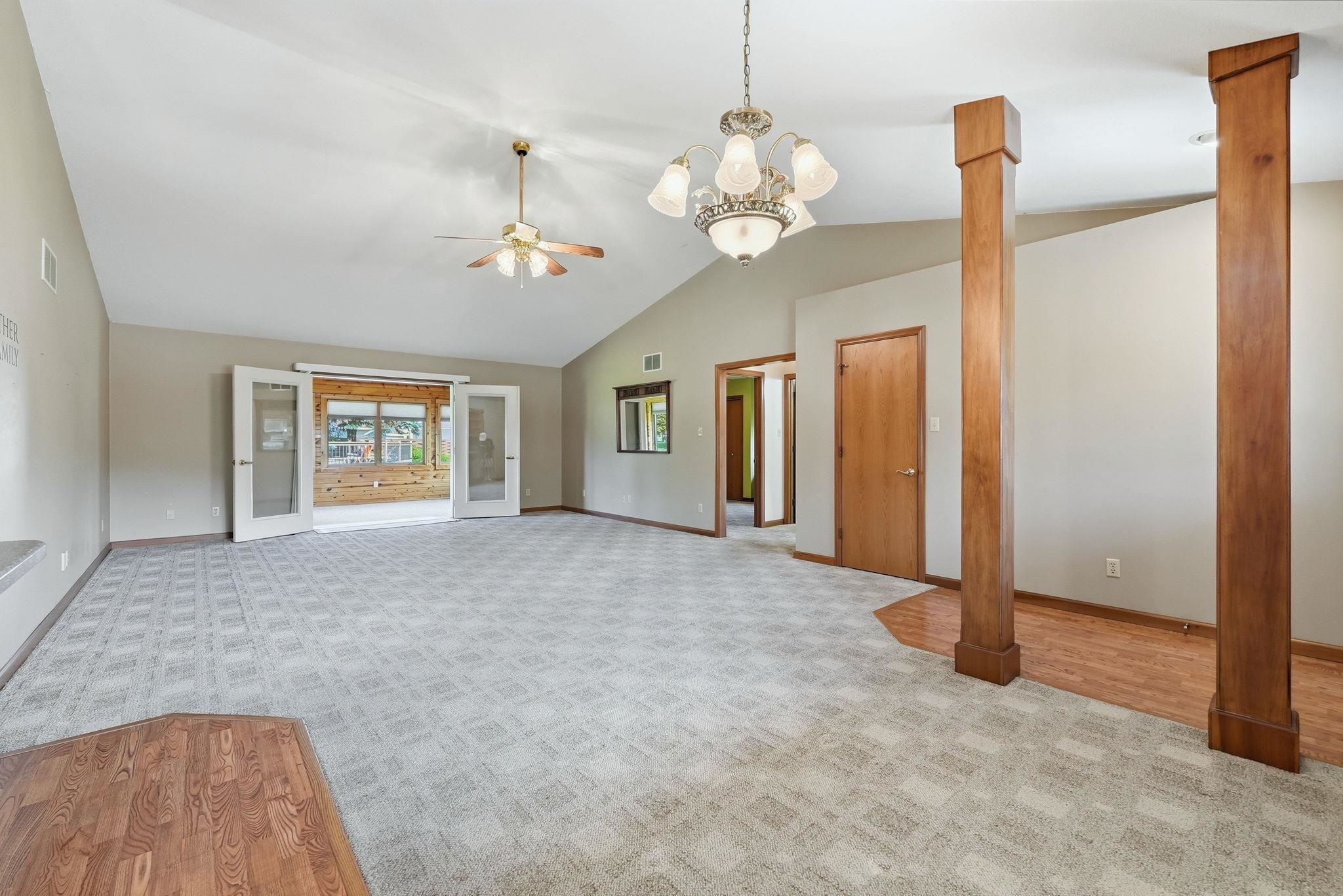 Spacious room featuring vaulted ceilings, patterned carpet flooring, a ceiling fan, and a chandelier