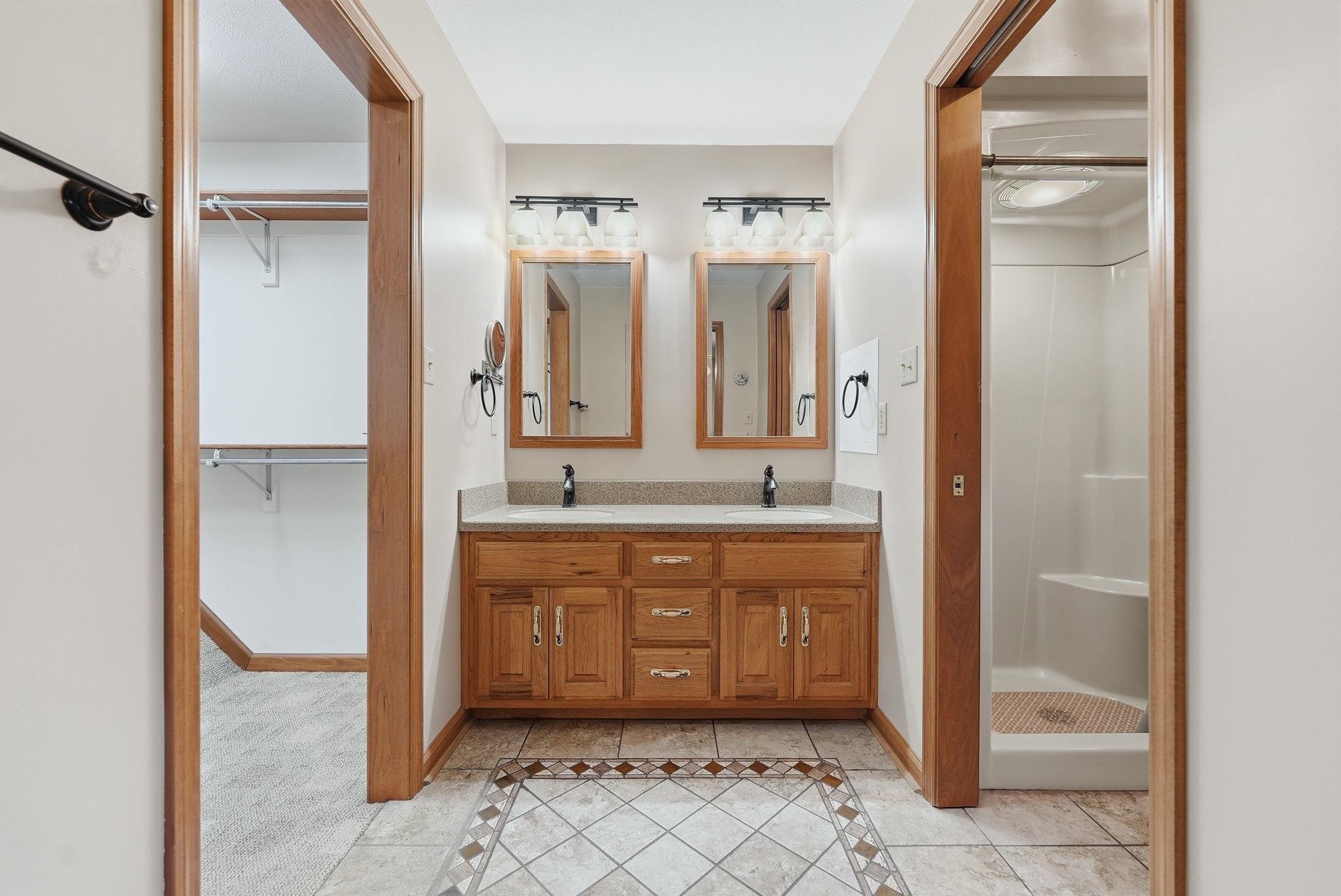 Dual vanity with light wood cabinetry, stone-look countertop, and individual framed mirrors