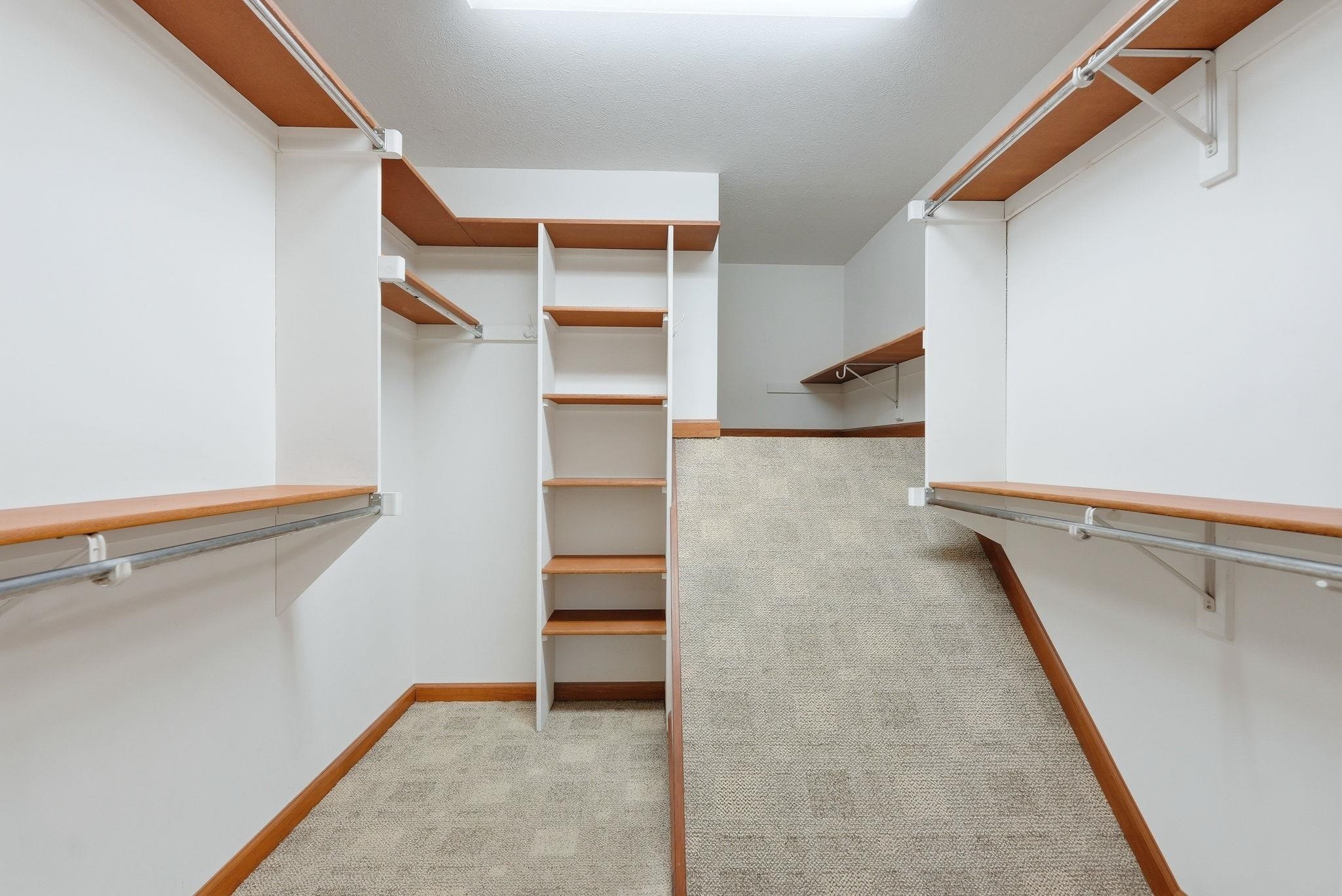 Expansive closet featuring white walls, wood-finish shelving, metal hanging rods, and patterned carpet flooring