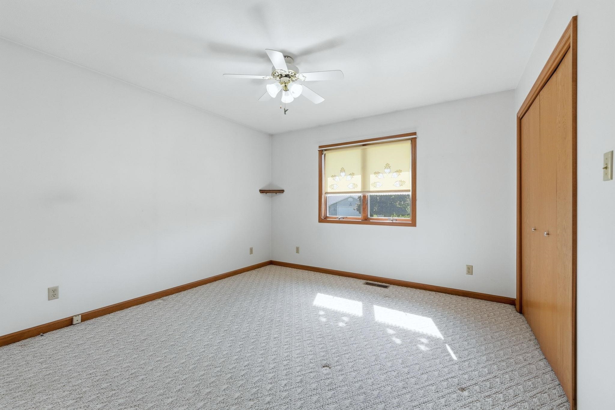 Carpeted room featuring a ceiling fan, a window with wood trim, a corner shelf, and a wood bi-fold closet door