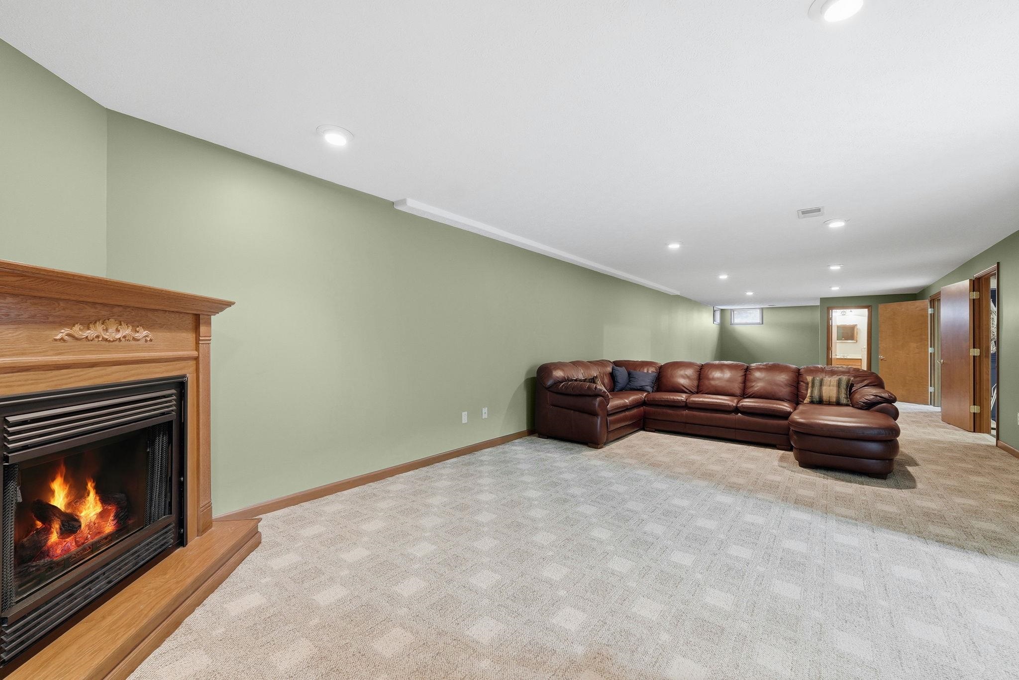 Spacious room featuring a fireplace with a wood mantle, recessed lighting, light green walls, light-colored patterned carpet, and wood trim