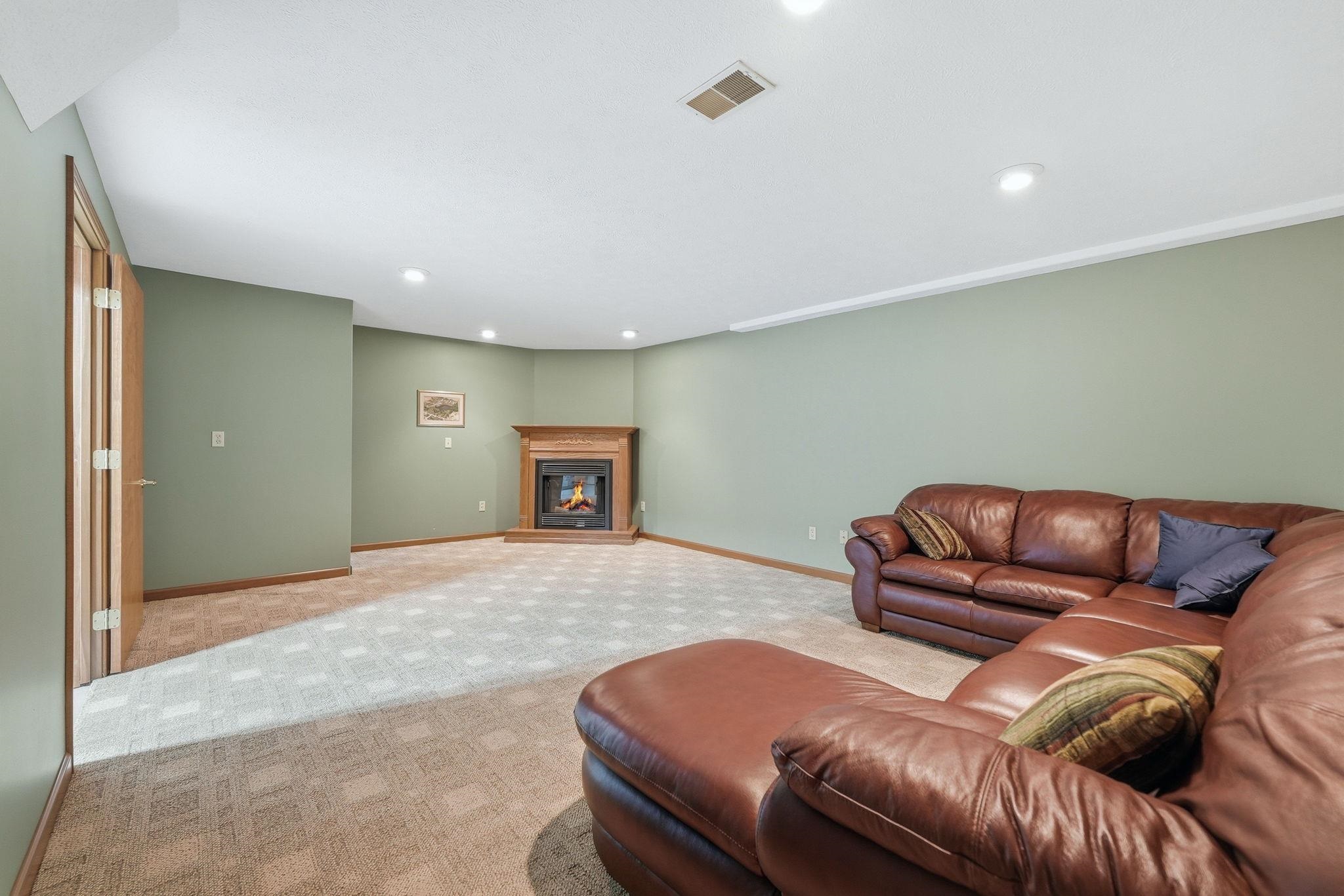Recessed lighting illuminates a carpeted room featuring a corner fireplace with a wood mantel