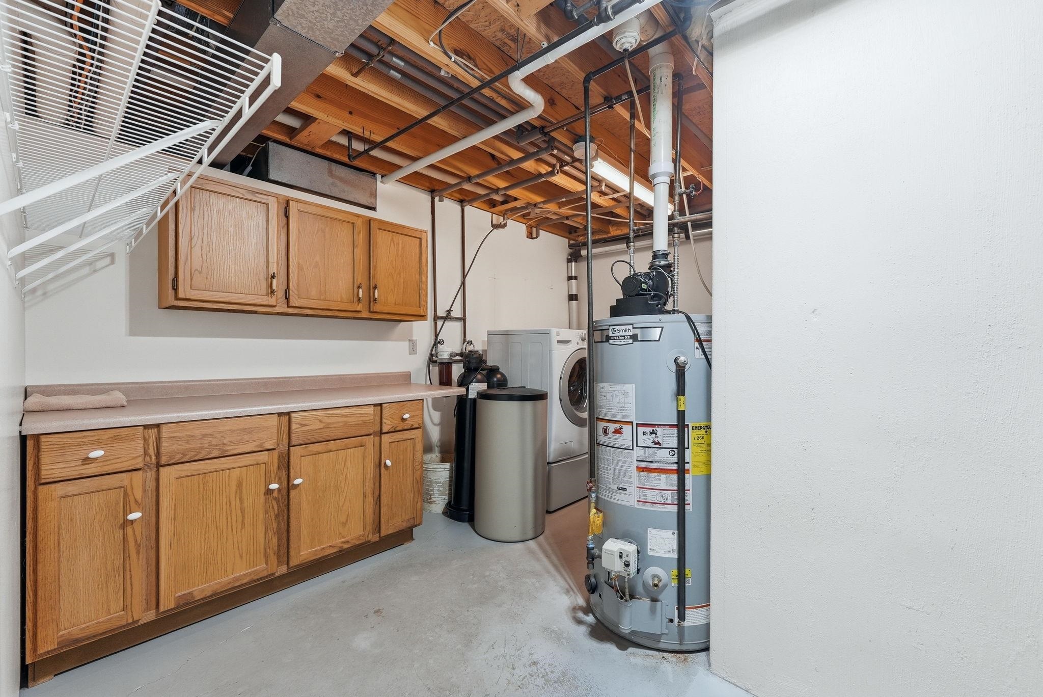 Laundry area featuring light wood-finish cabinetry, a neutral countertop, white wire shelving, a front-loading washing machine, and a water heater